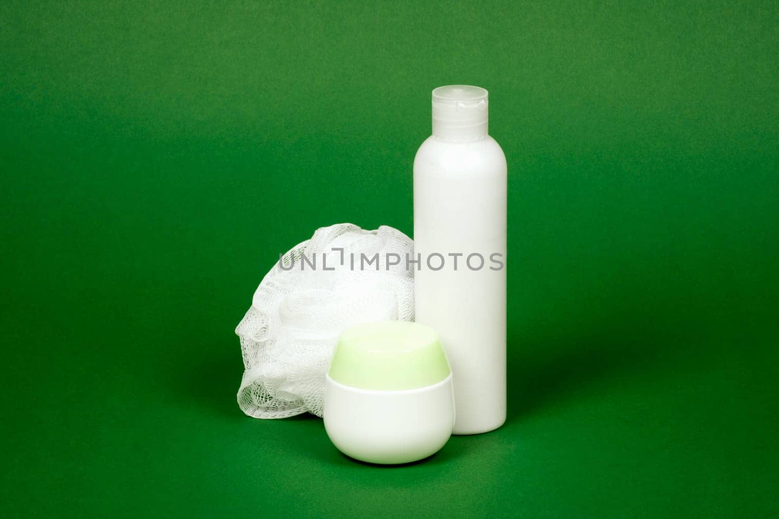 White tube of shower gel and white bath sponge are on green background.