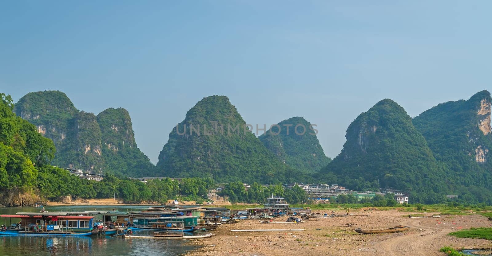 Yangshuo, China - August 2019 : Panoramic view of the OLi river shore with small tourist and fishermen boats on the riverbank, the ferry crossing point in Yangshuo town, Guangxi Province