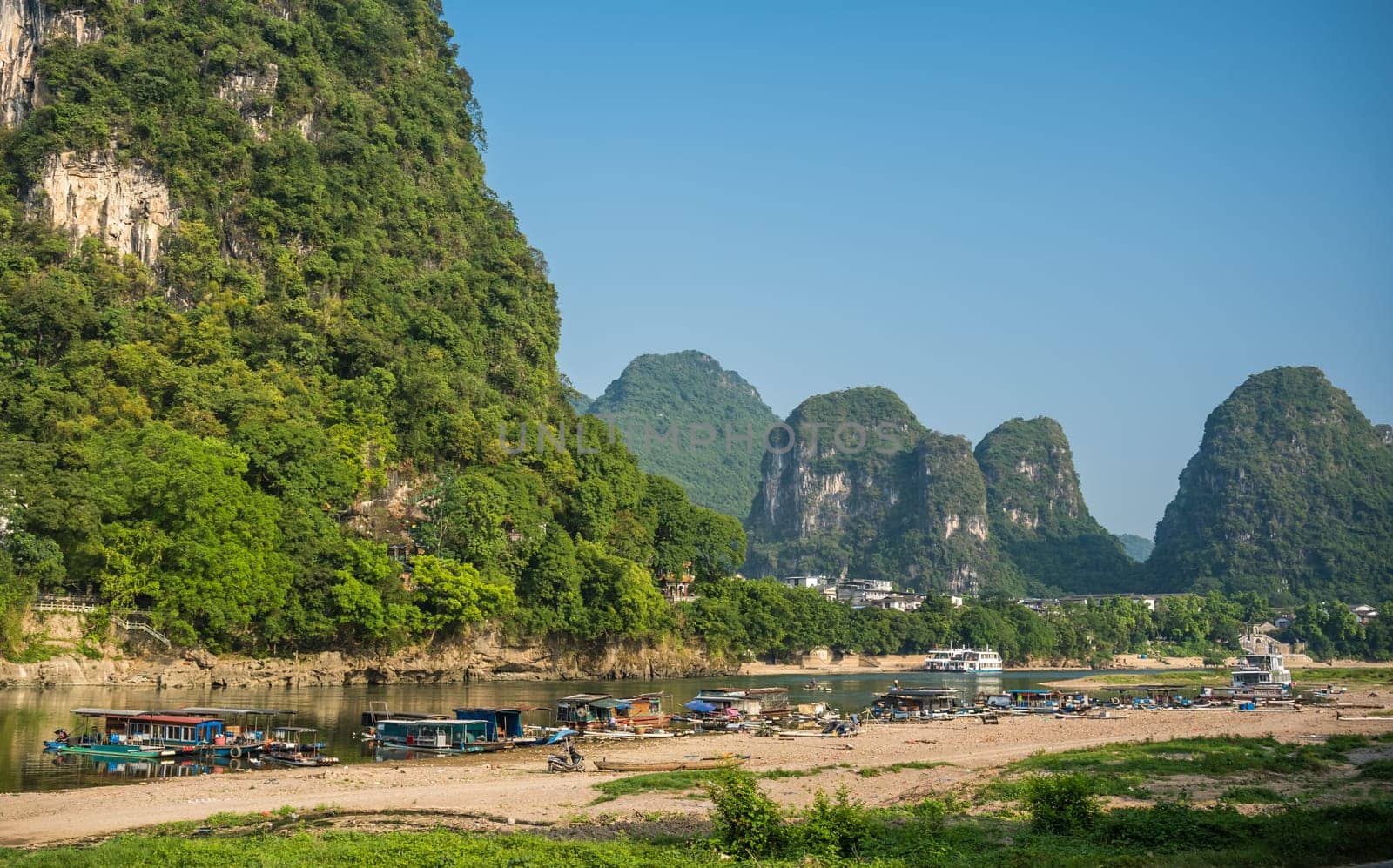 Yangshuo, China - August 2019 : Panoramic view of the OLi river shore with small tourist and fishermen boats on the riverbank, the ferry crossing point in Yangshuo town, Guangxi Province