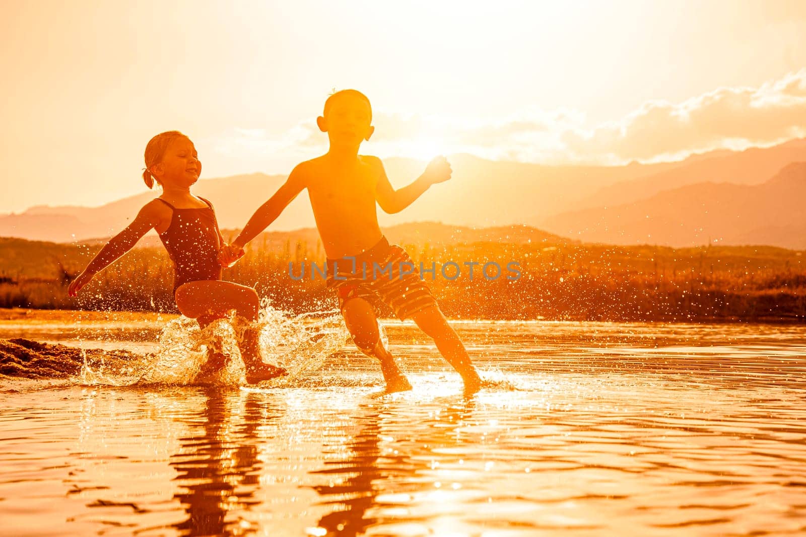 portrait of two children aged 3 and 6 playing in the sea and spraying water around them. Backlight image at sunset