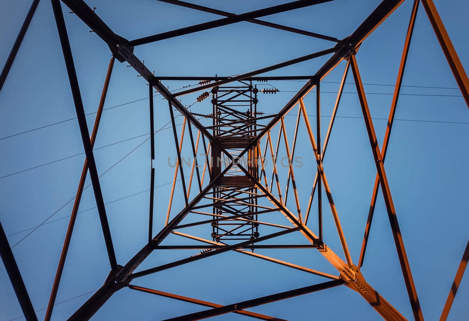 Underneath a truss pillar construction. Different geometric shapes, patterns of a steel structure. Metallic texture of an electricity pole.