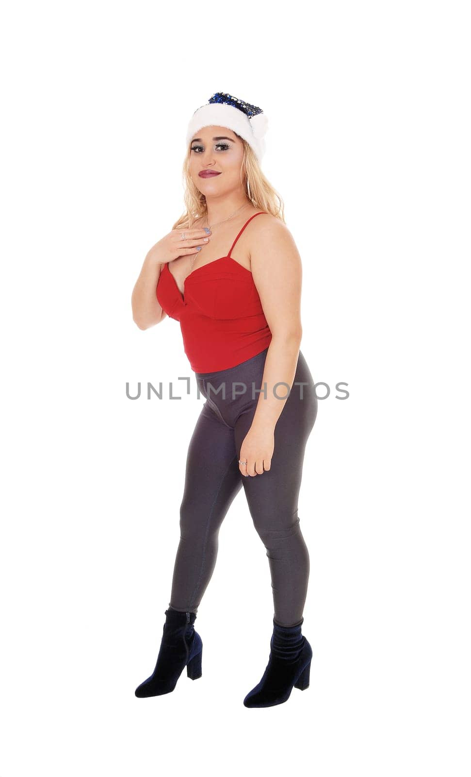 A beautiful young woman standing in profile in gray tights and.red top with a Santa hat, isolated for white background.