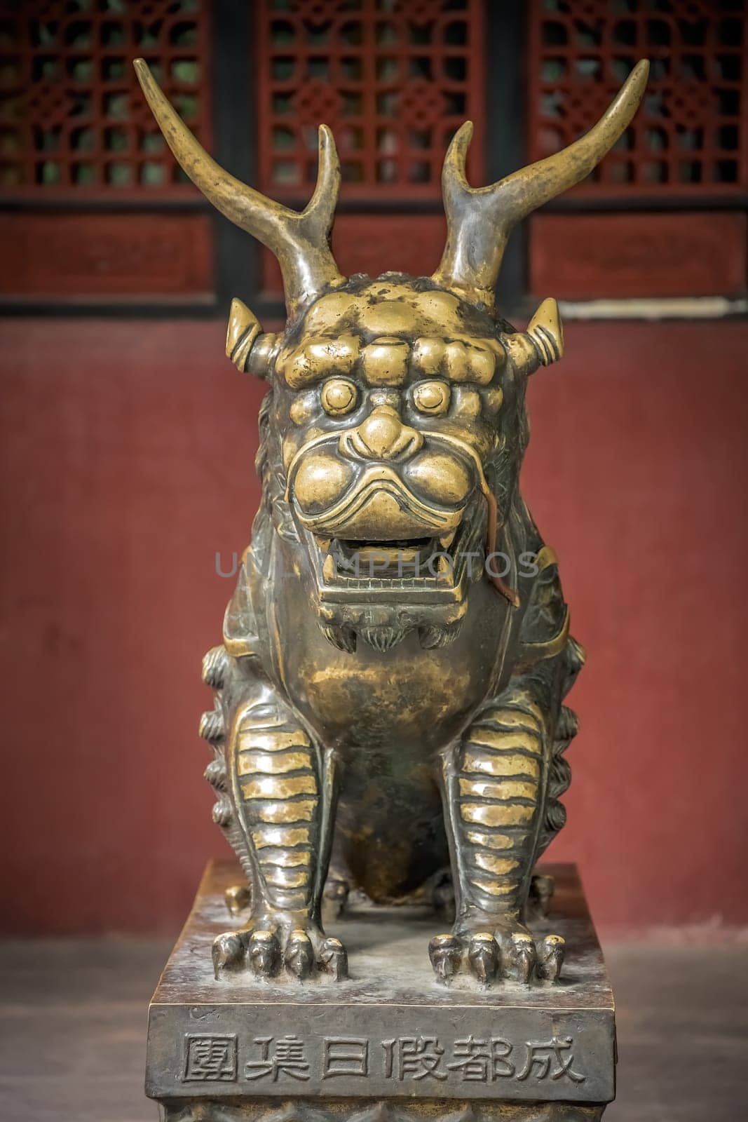 Statue of mystical Chinese golden brass guardian lion on red wall background in the courtyard of the Buddhist Wenshu Temple Monastery, Chengdu, Sichuan Province, China