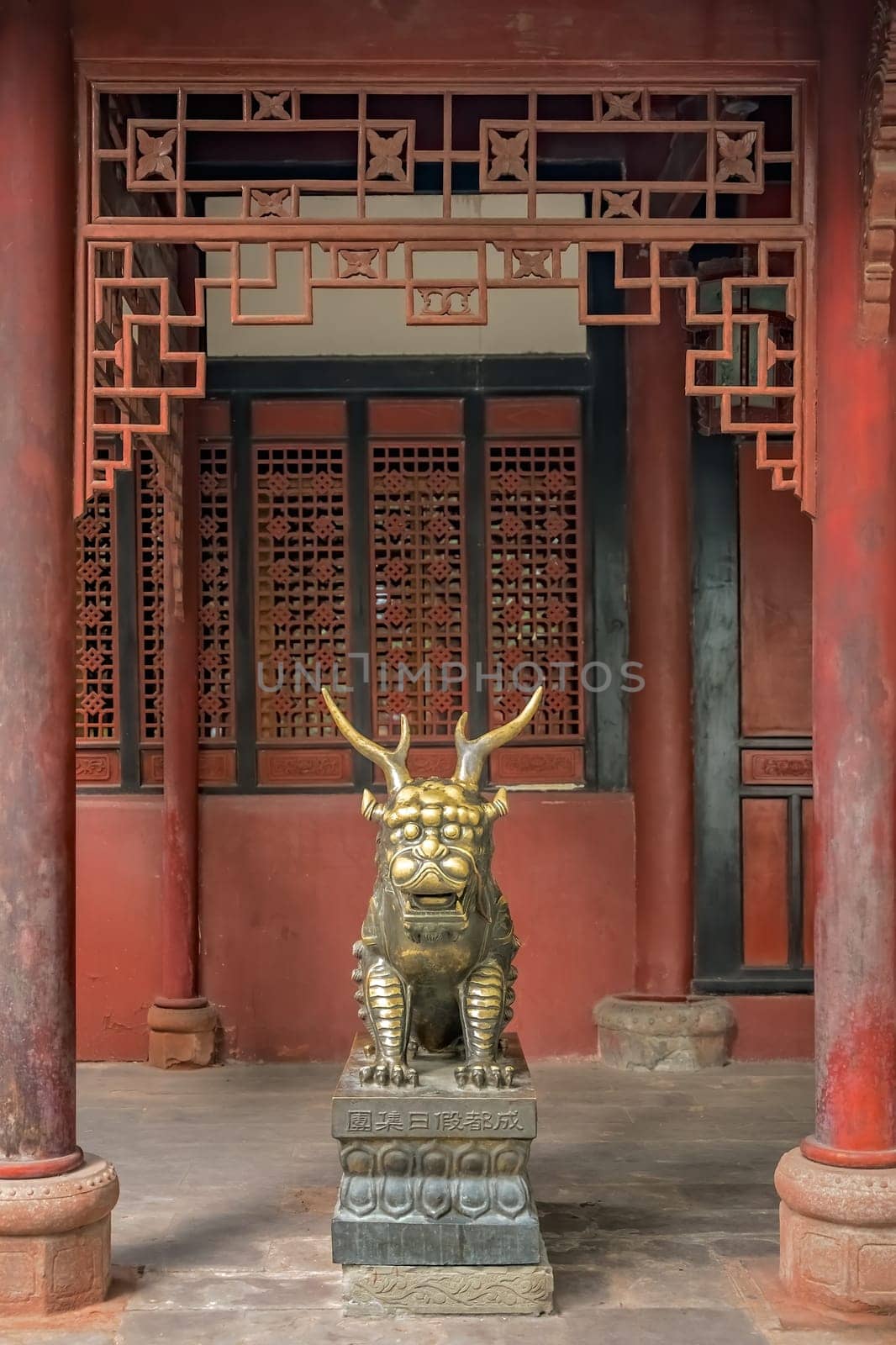 Statue of mystical Chinese golden brass guardian lion on red wall background in the courtyard of the Buddhist Wenshu Temple Monastery, Chengdu, Sichuan Province, China