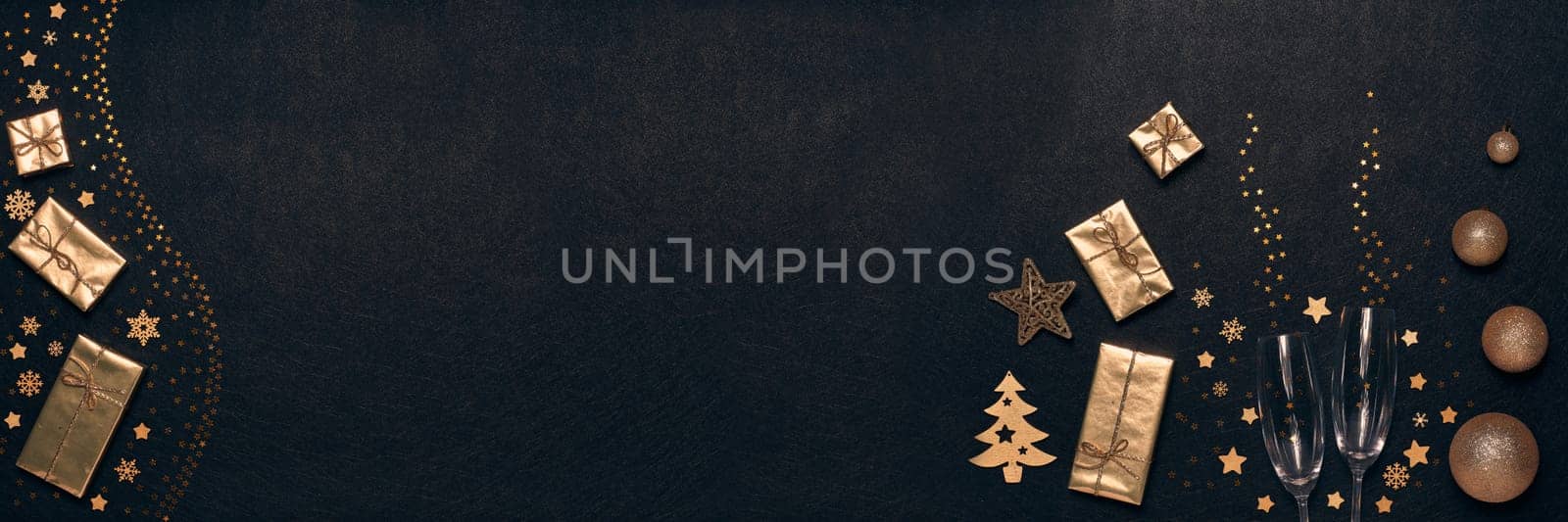 Golden Christmas decorations, gift boxes, champagne flutes on black background. Top view, copy space. Design element for greeting card, invitation, advertising. Extra wide panorama banner background