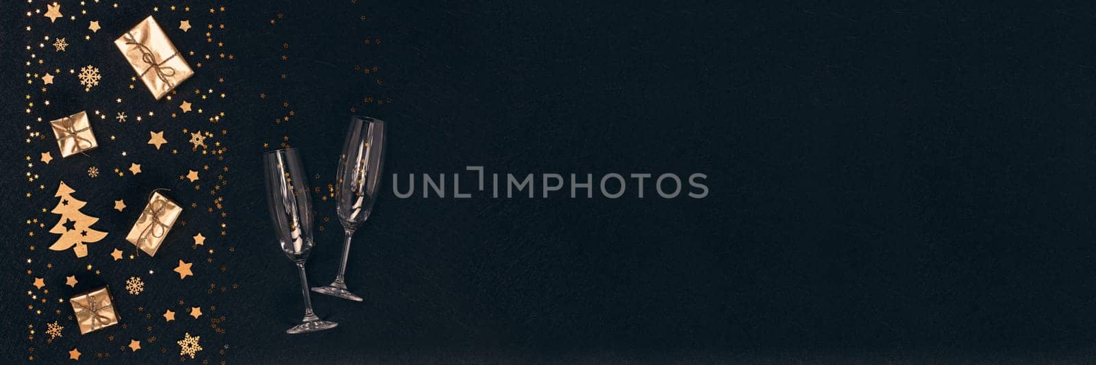 Golden Christmas decorations, gift boxes, champagne flutes on black background. Top view, copy space. Design element for greeting card, invitation, advertising. Extra wide panorama banner background