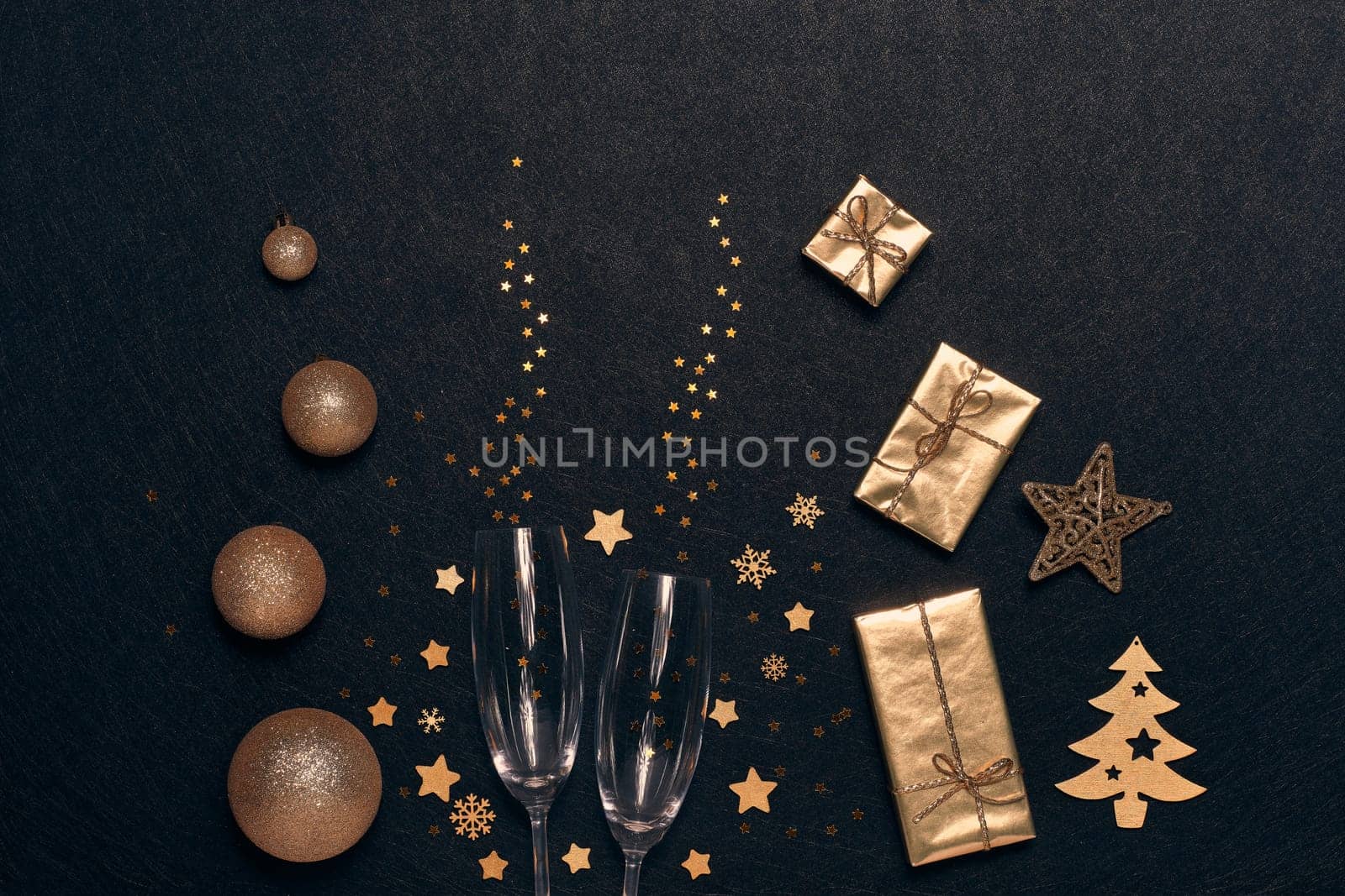 Festive composition with golden Christmas decorations, gift boxes, empty champagne flutes on black background. Top view. Design element for greeting card, invitation, advertising