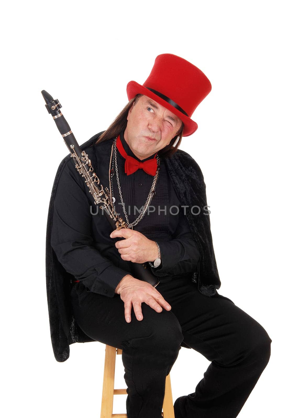 A middle age indigenous man holding his clarinet in a black outfit and.red hat and bow tie looking away, isolated for white background.
