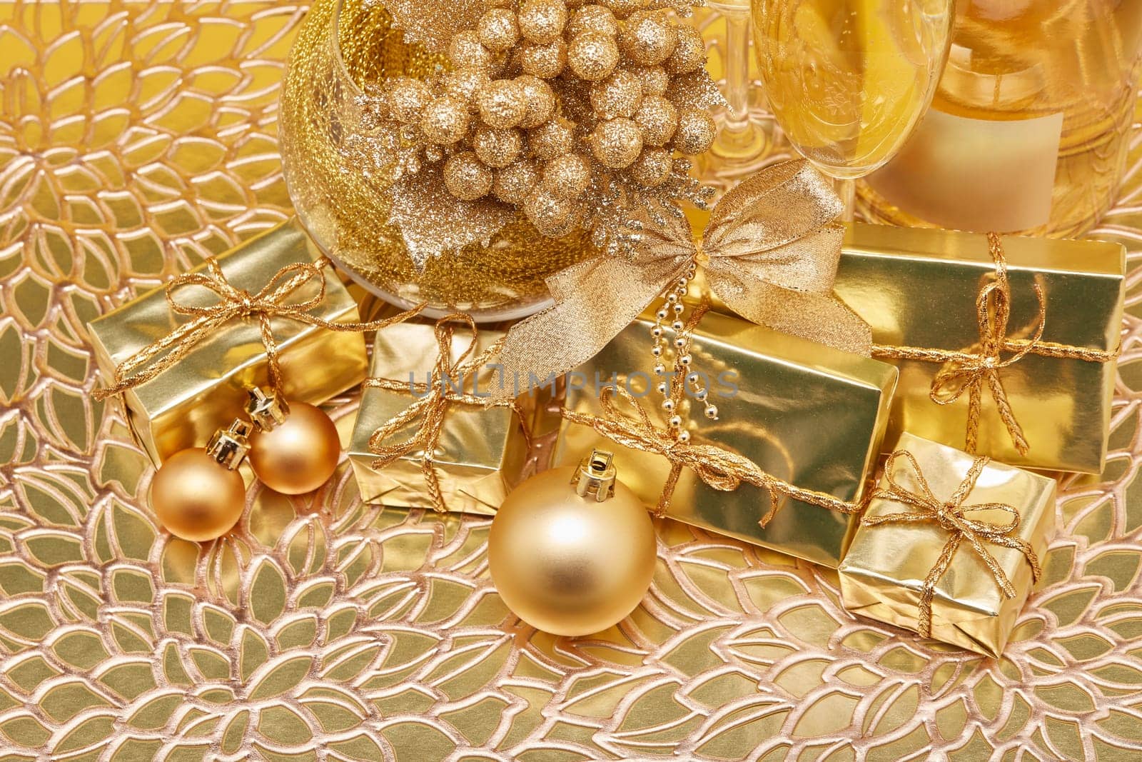 Golden Christmas ornaments, gift boxes, champagne bottle and full champagne flutes on gold background. Christmas. New Year. Design element for greeting card, invitation, advertising