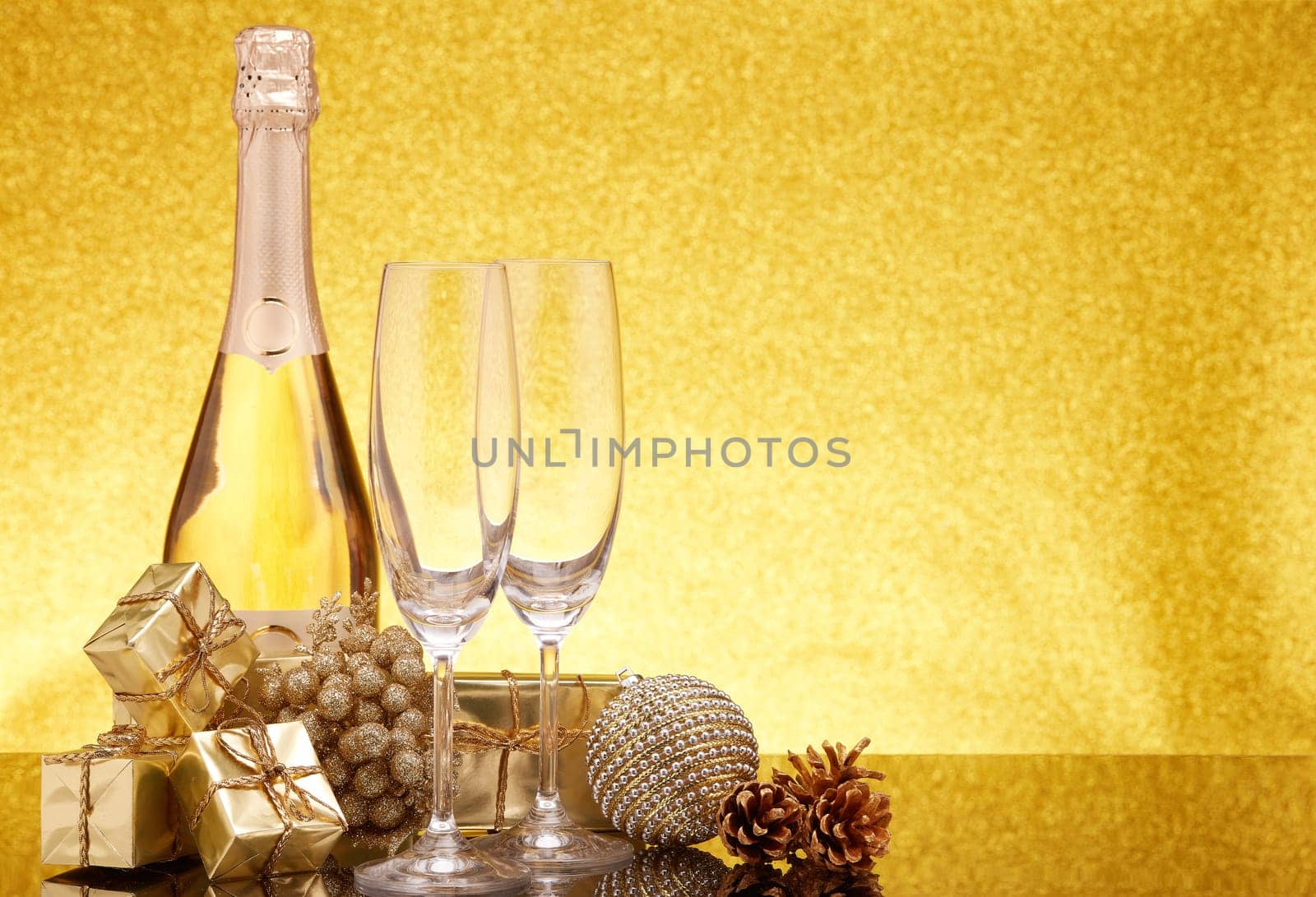 Golden Christmas ornaments, gift boxes, champagne bottle and empty champagne flutes on gold background with copy space. Christmas. New Year. Design element for greeting card, invitation, advertising
