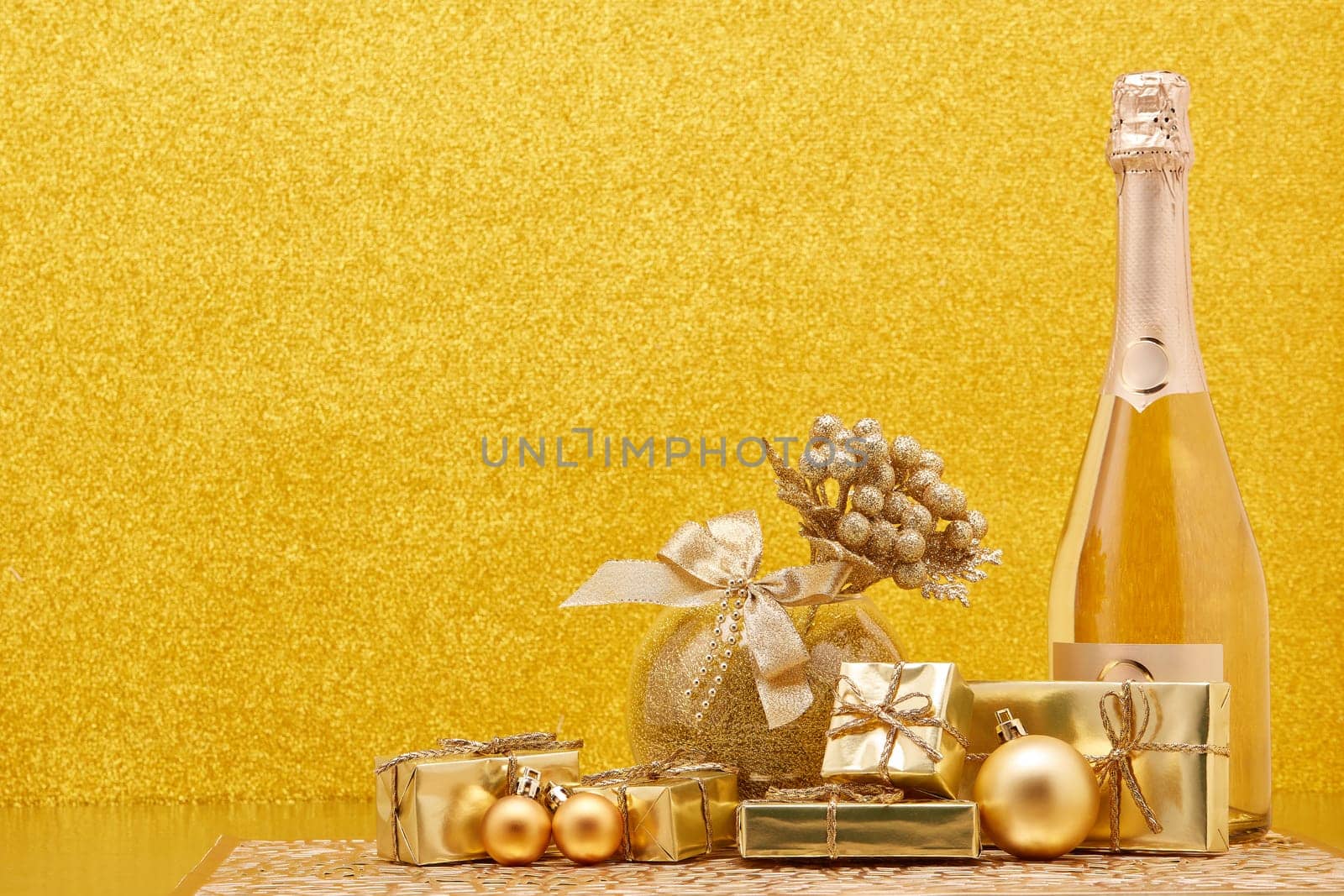 Golden Christmas ornaments, gift boxes and champagne bottle on gold background with copy space. Christmas. New Year. Design element for greeting card, invitation, advertising