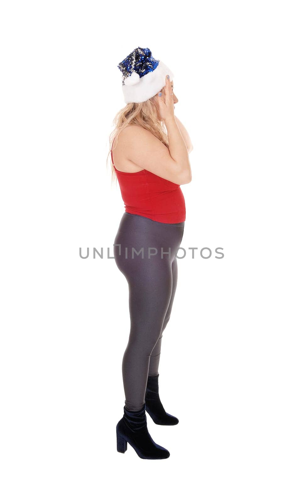 A beautiful young woman standing in profile in black tights and.red top with a Santa hat, isolated for white background.