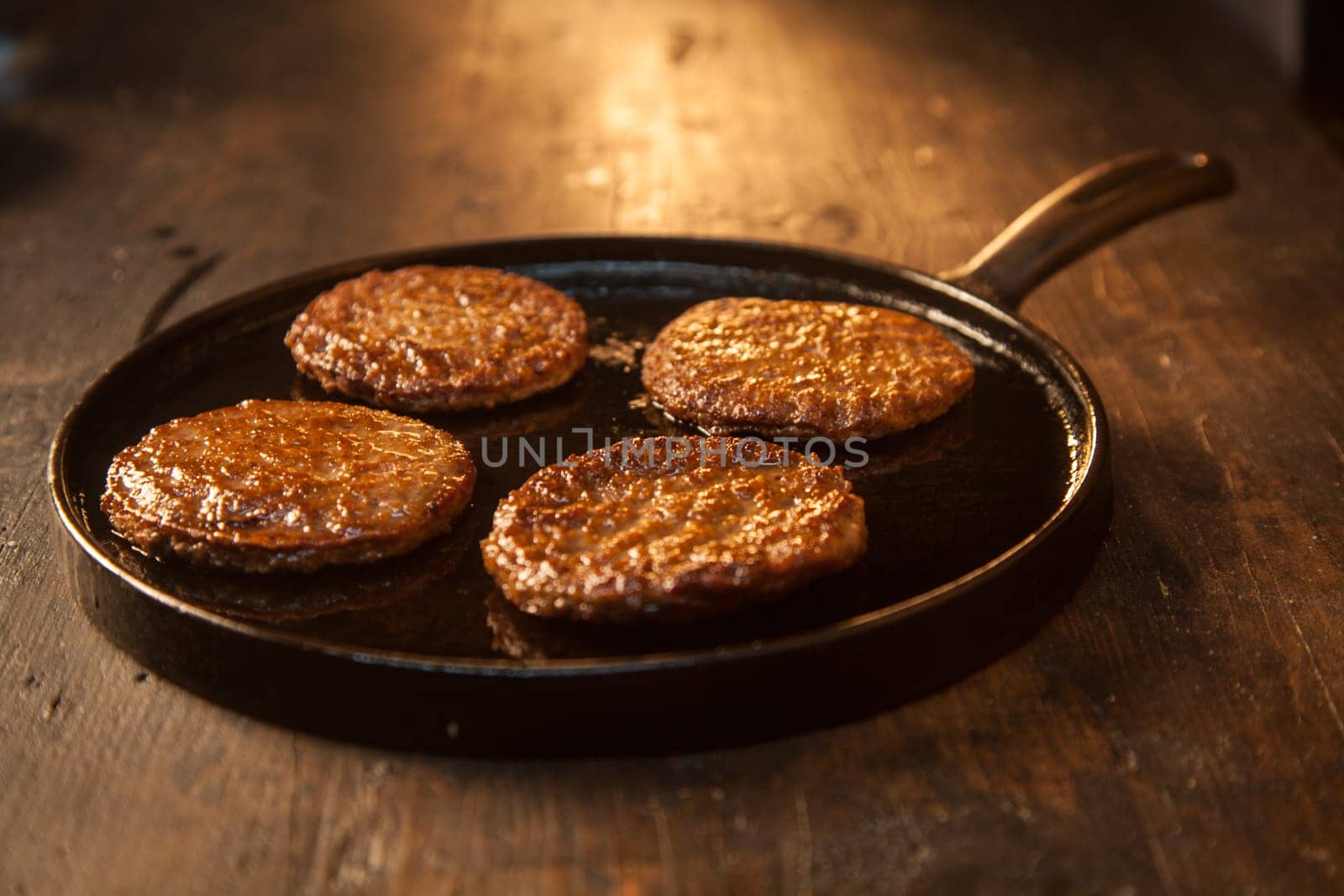 Four tasty meat patties or frikadeller made from a mixture of ground beef, pork or veal in an old metal skillet on a wooden counter , low angle view