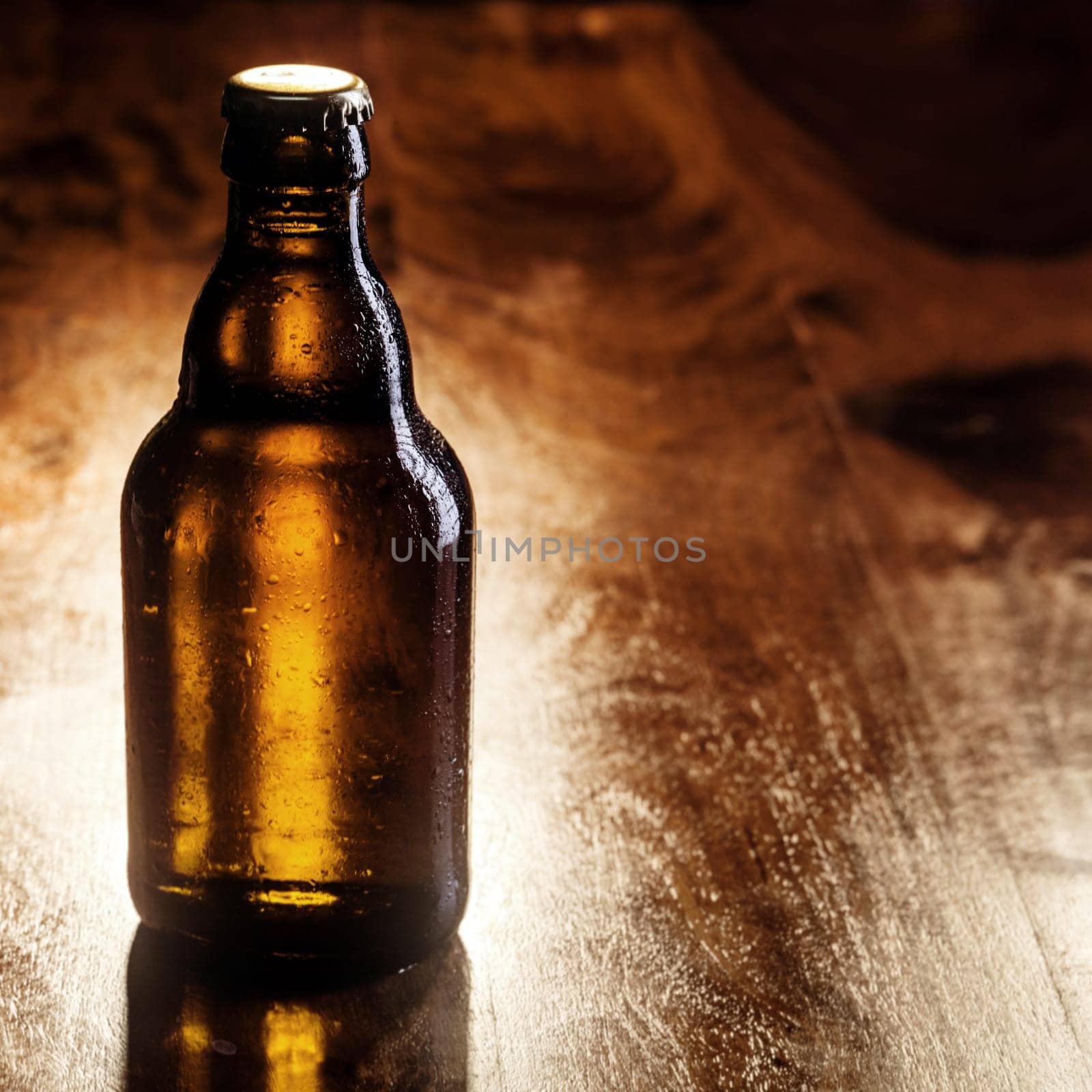 Unlabeled unopened brown bottle of cold beer standing on a wooden bar counter with copyspace for your advertising
