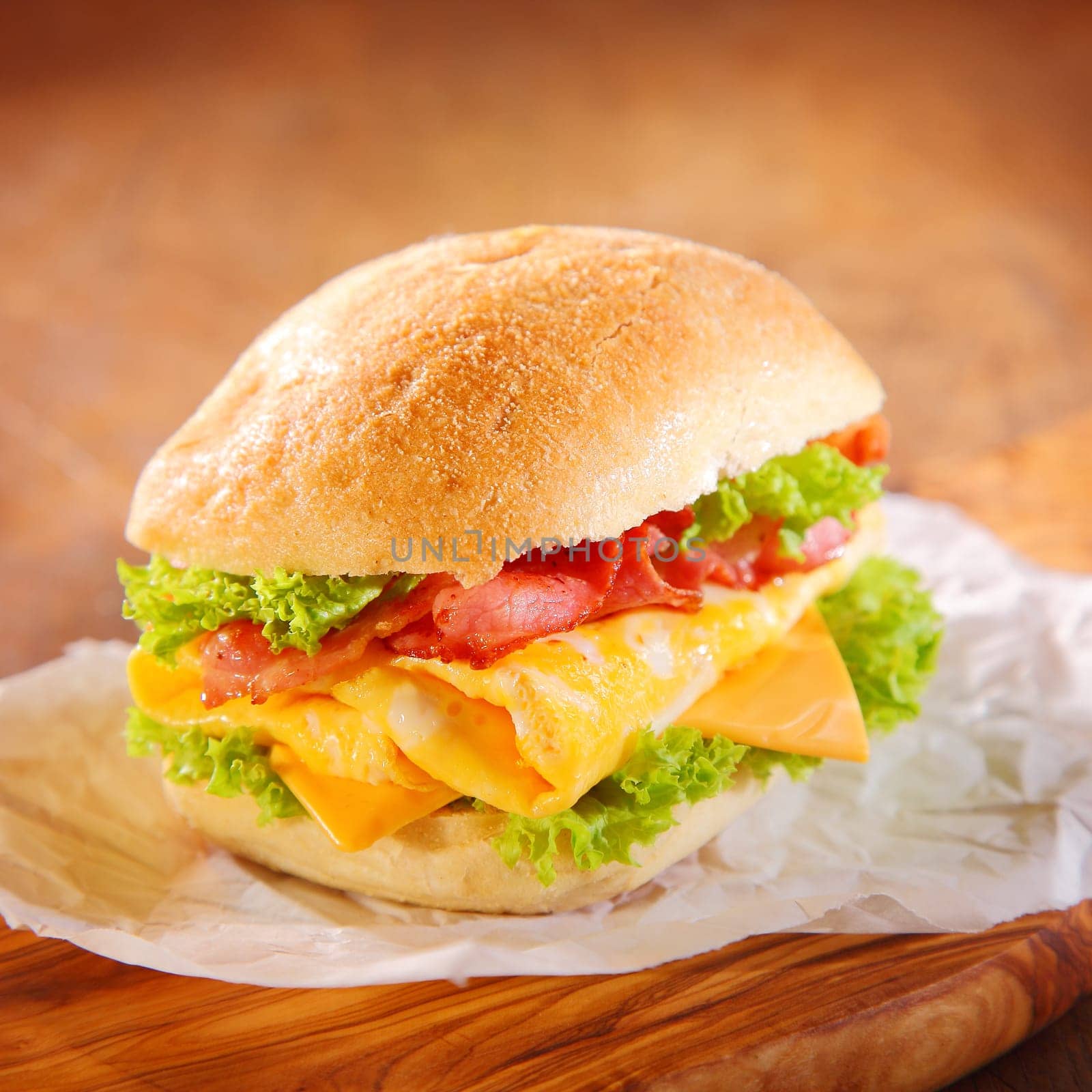 Tasty homemade hamburger filled with slices of pork ham, cheese and green fresh salad or lettuce, served on a paper, on a rustic wooden table