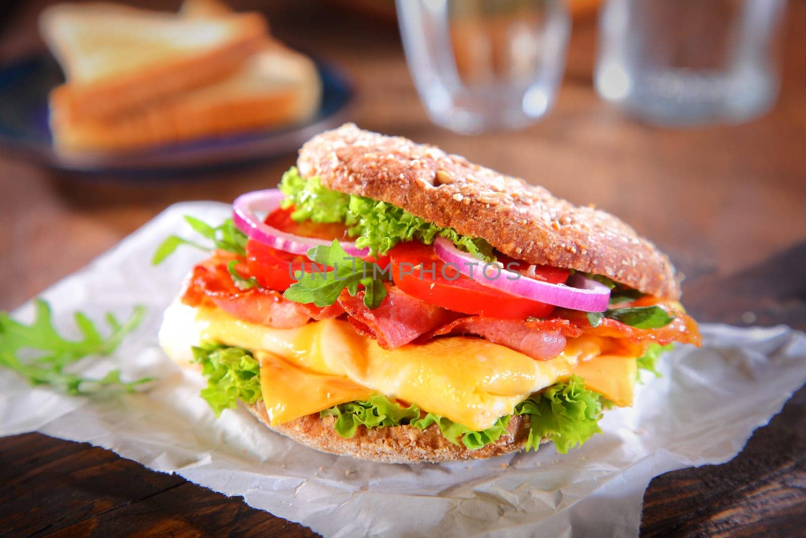 Tasty Fresh Burger with Bacon and Cheese, Added with Lettuce, Onions and Tomatoes, on White Paper Above Wooden Table.