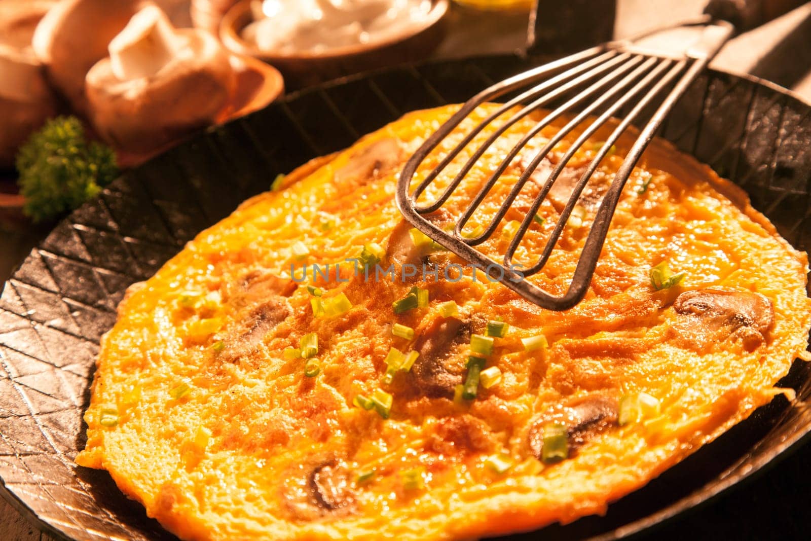 Tasty egg omelette with sliced fresh mushrooms and aromatic herbs in an old pan with a lifting spatula balanced above ready to be served