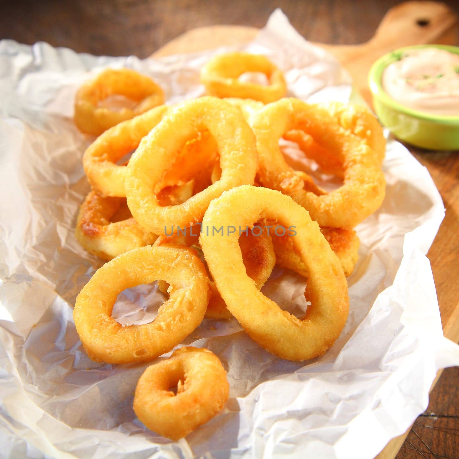 Salty and crispy fried squid rings served on a paper with wasabi mayonnaise, on a wooden cutting board