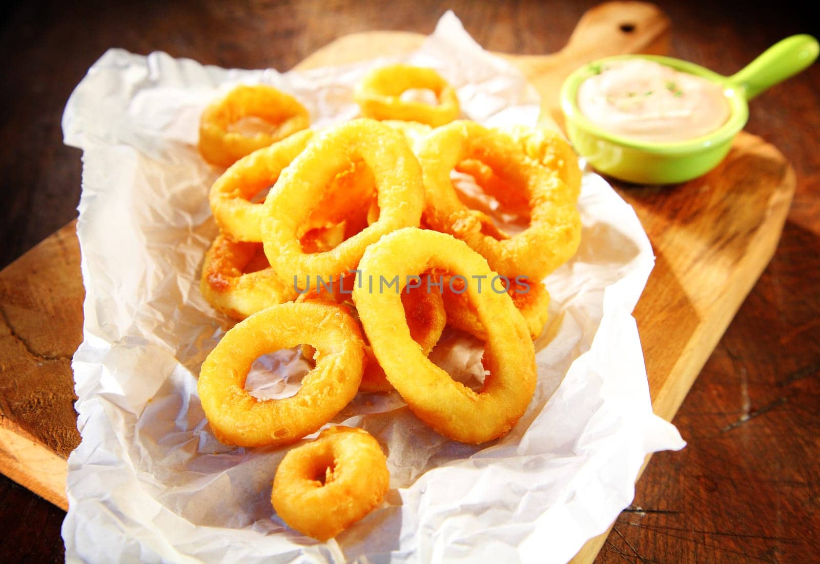 Close up Tasty Fried Squid Rings with Sour Cream Sauce on White Paper Above Wooden Serving Board.