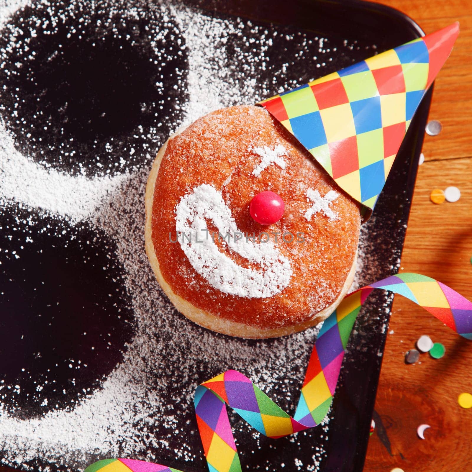 Close up Carnival Doughnut on Black Tray with Hat and Confetti Decoration with Round Shapes on Side Formed from Icing Sugar.
