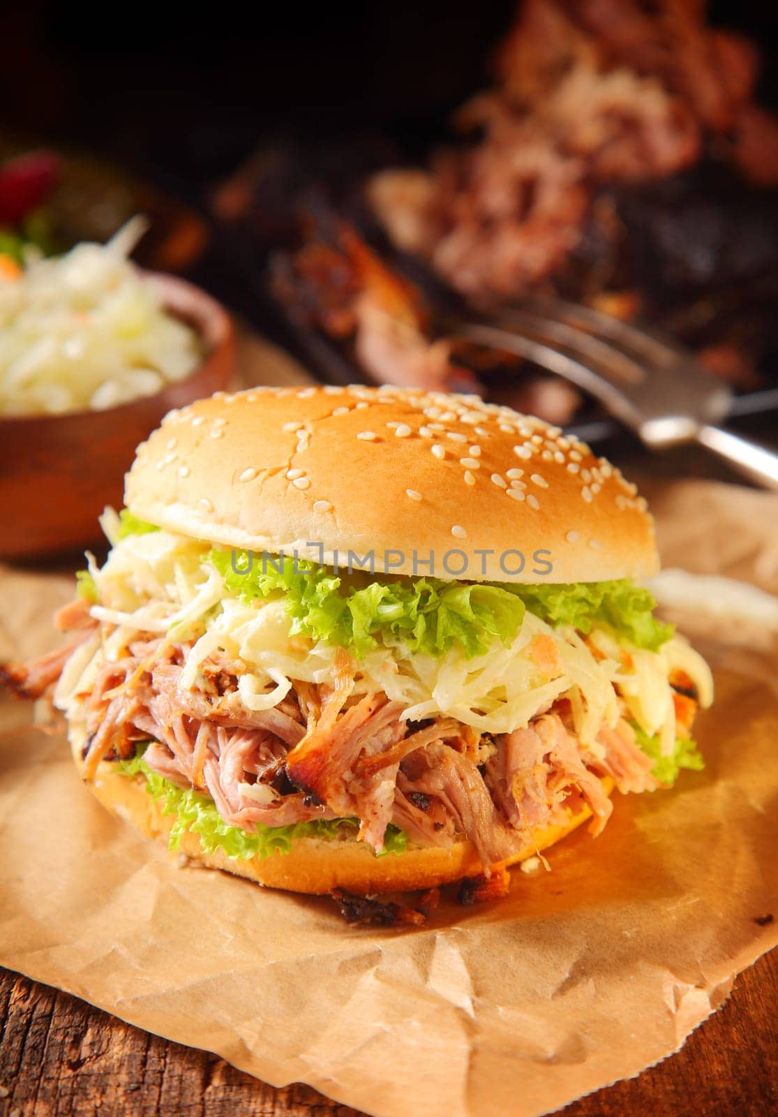 Close up Gourmet Pulled Pork Burger on Brown Paper, Placed on Wooden Table with Other Dishes.