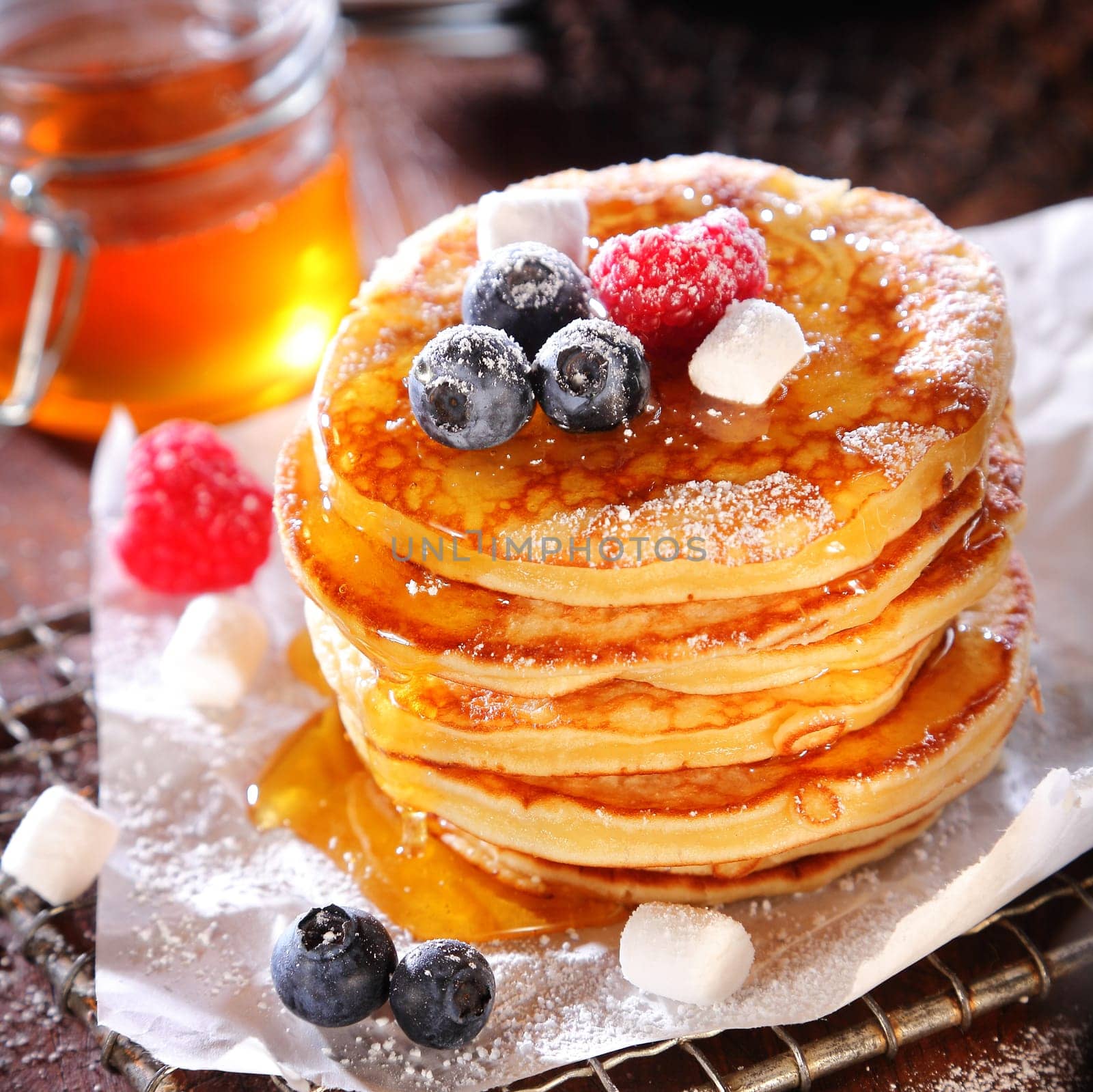 Delicious breakfast of fruity berry pancakes pile in a stack and drizzled with syrup and sugar with fresh blueberries and raspberries