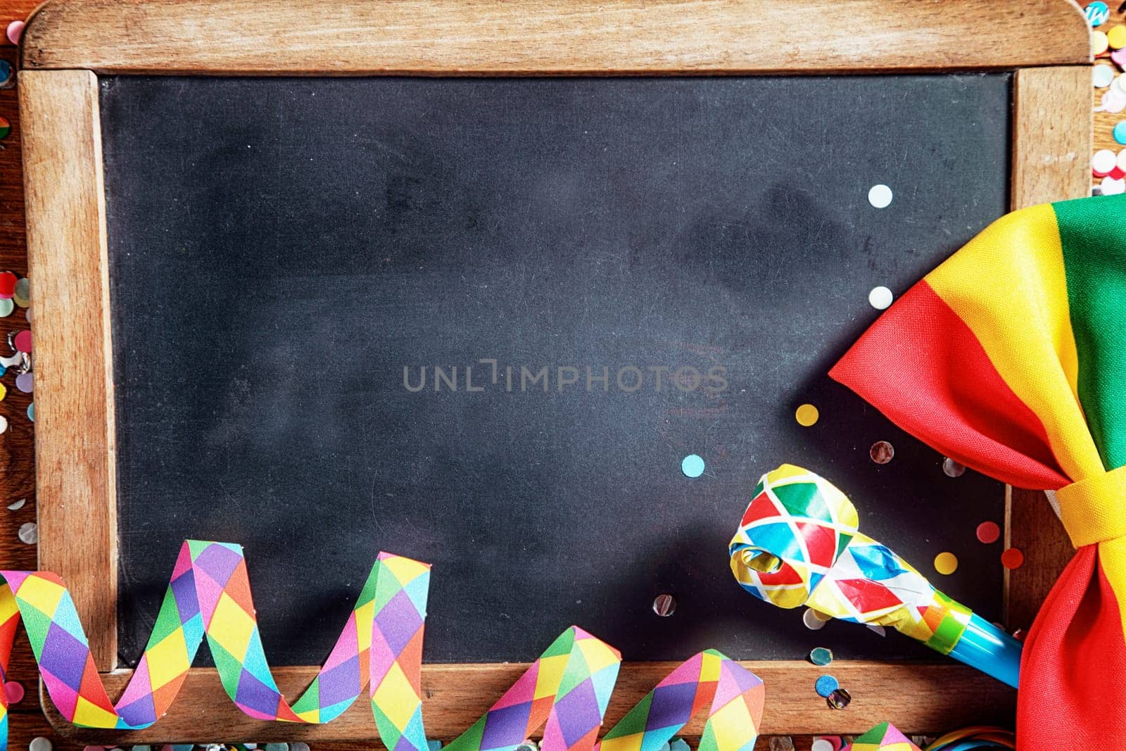 Close up Colorful Carnival Paper Streamers, Whistle and Ribbon in Front Empty Black Board. Emphasizing Copy Space.