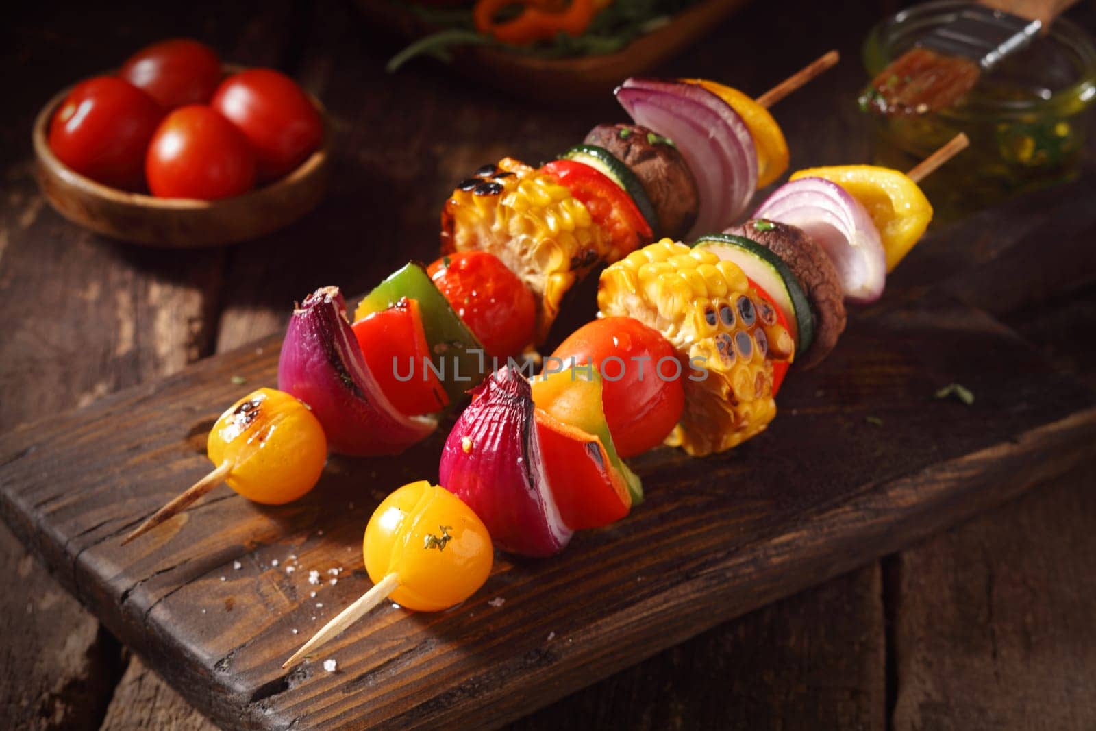 Colorful vegan or vegetarian vegetable skewers with fresh roasted or grilled sweet peppers, onion, mushroom, corn, eggplant and cherry tomatoes, close up view on a wooden board