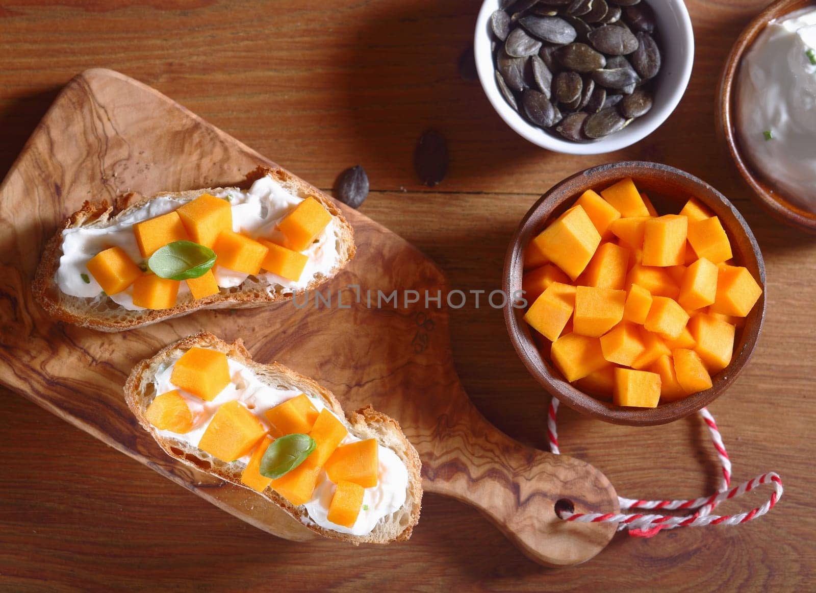 Close up Aerial Shot of Healthy Creamed Bread with Filling on Top of Wooden Cutting Board with Bowl of Carrot Slices and Pumpkin Seeds on the Side.