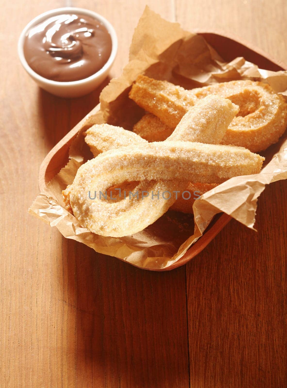 Close up Delicious Churros Snacks on Tray, with Paper, with Chocolate Dipping Sauce on Side. Placed on Wooden Table.