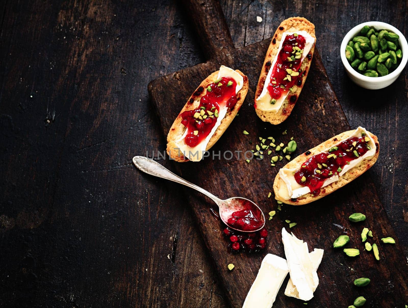 Delicious Sliced Bread with Cheese and Cranberry Sauce on Wooden Serving Board on Top of Dark Wooden Table.