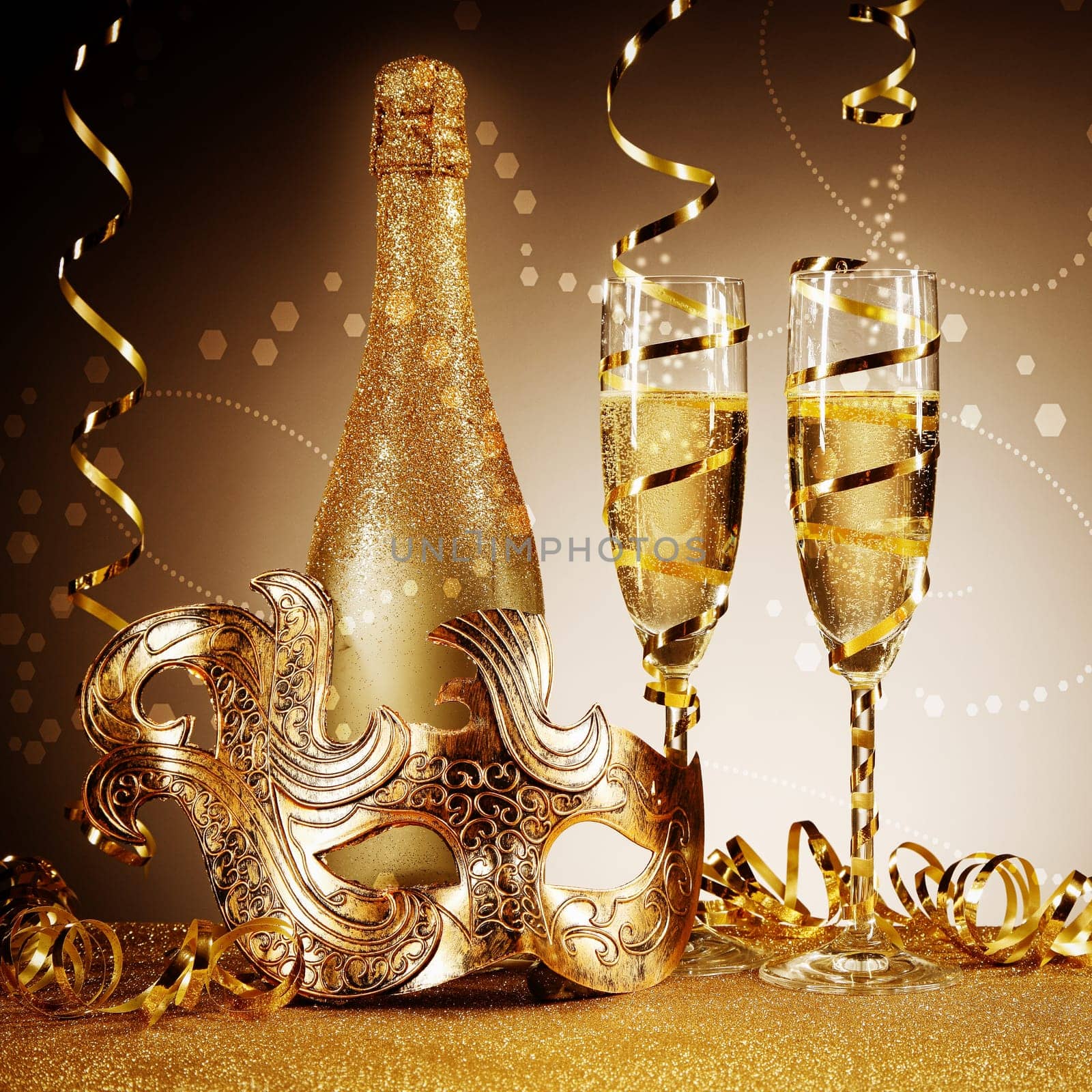 Close up Golden Party Wine Bottle and Glass with Masquerade Mask, Styled with Streamers on Glittery Table in Front Gradient Brown Background.