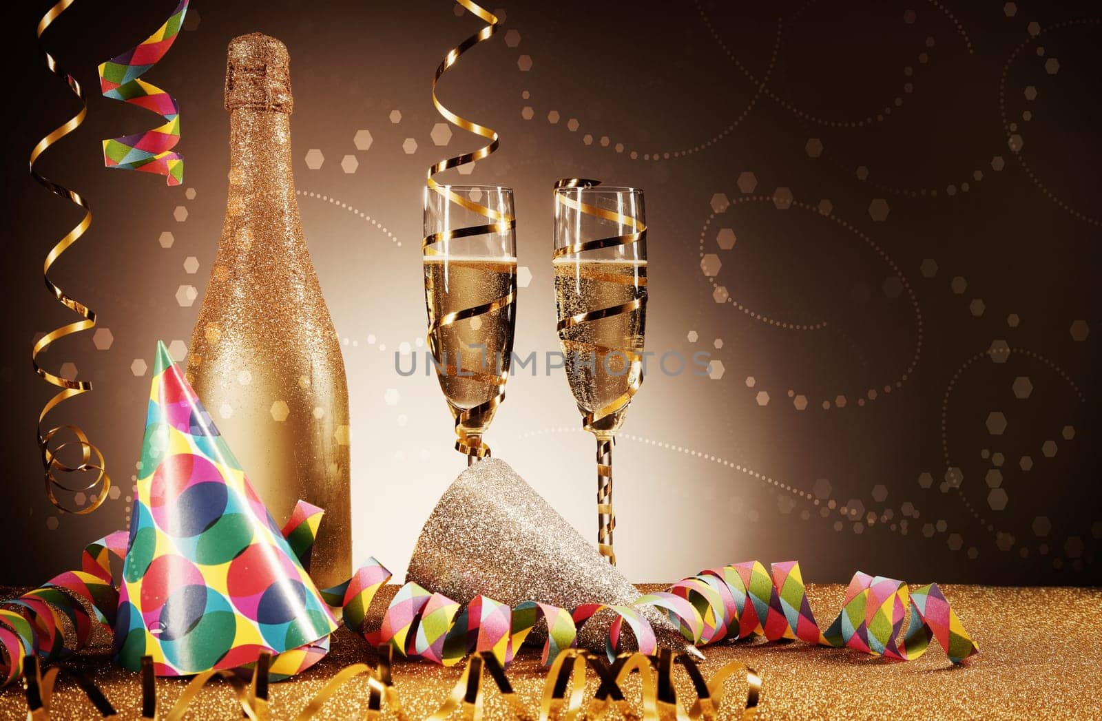 Festivity Concept - Close up Party Cone Hats, Golden Wine Bottle and Glass and Paper Streamers on Glittery Platform In Front Gradient Brown Background.