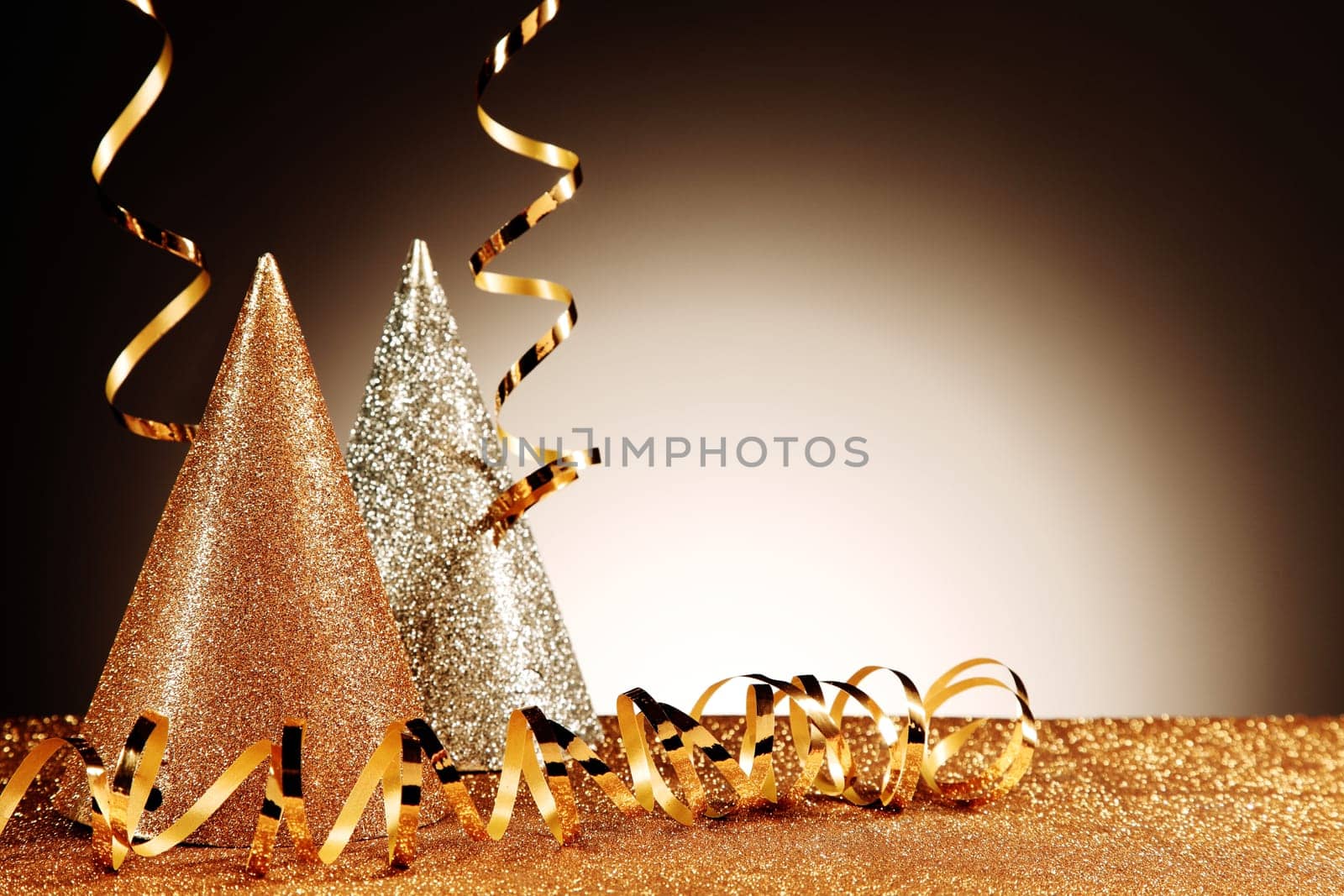 Close up Glittery Table with Glittery Silver and Gold Cone Hats and Streamers on Gradient Brown Background. Emphasizing Copy Space.
