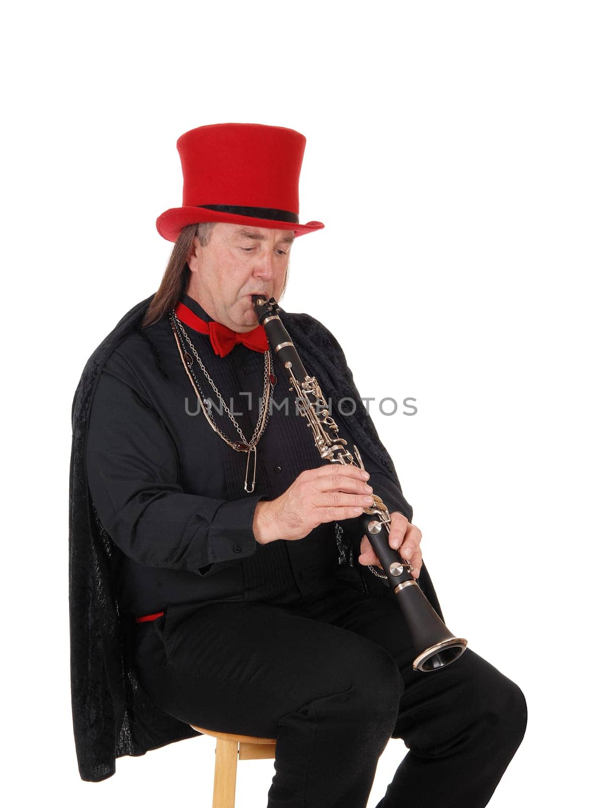 A middle age indigenous man playing his clarinet in a black outfit and.red hat and bow, isolated for white background.