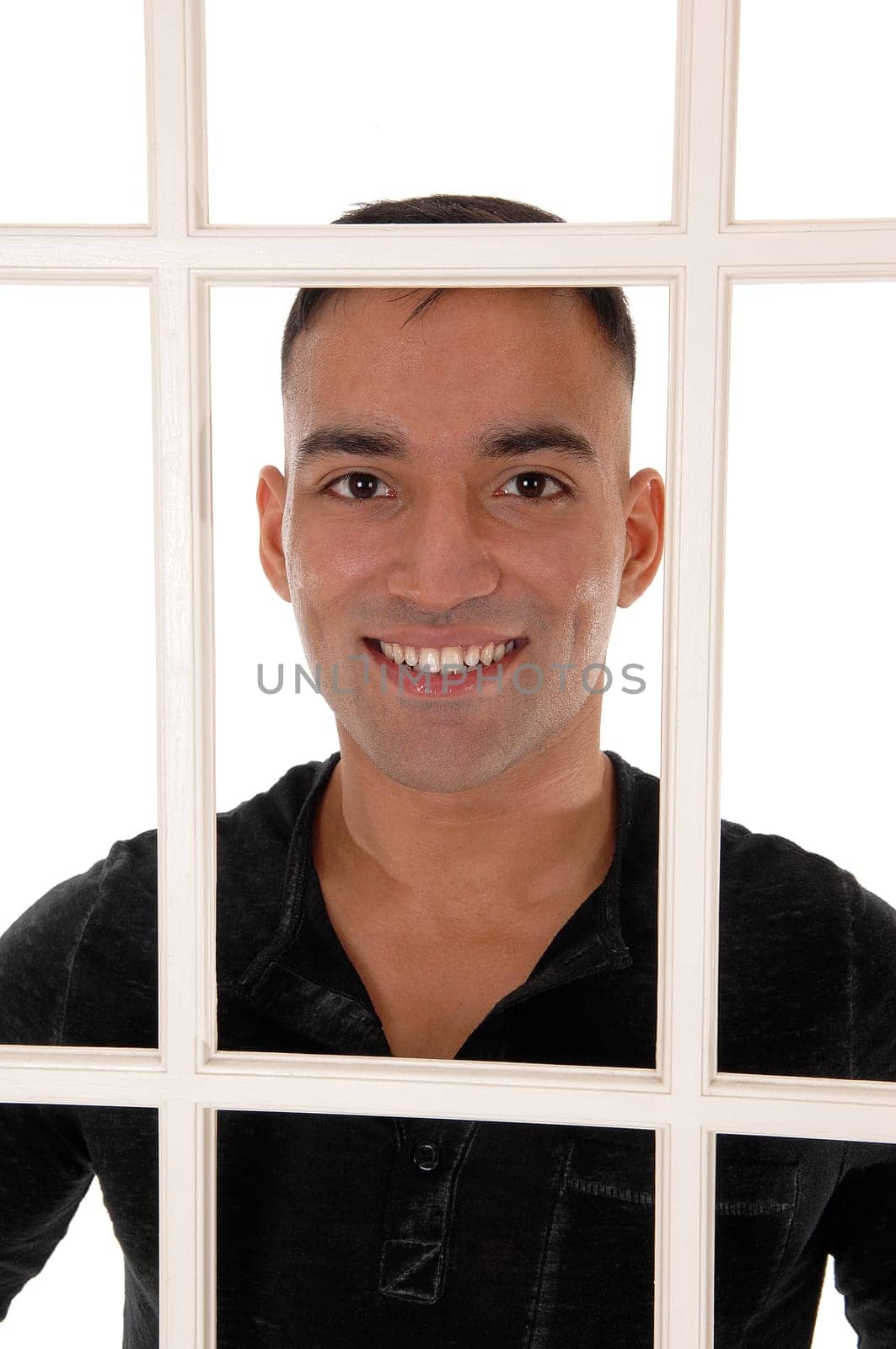 A happy east Indian man standing behind a white window frame in a.black dress shirt with a big smile, isolated for white background.