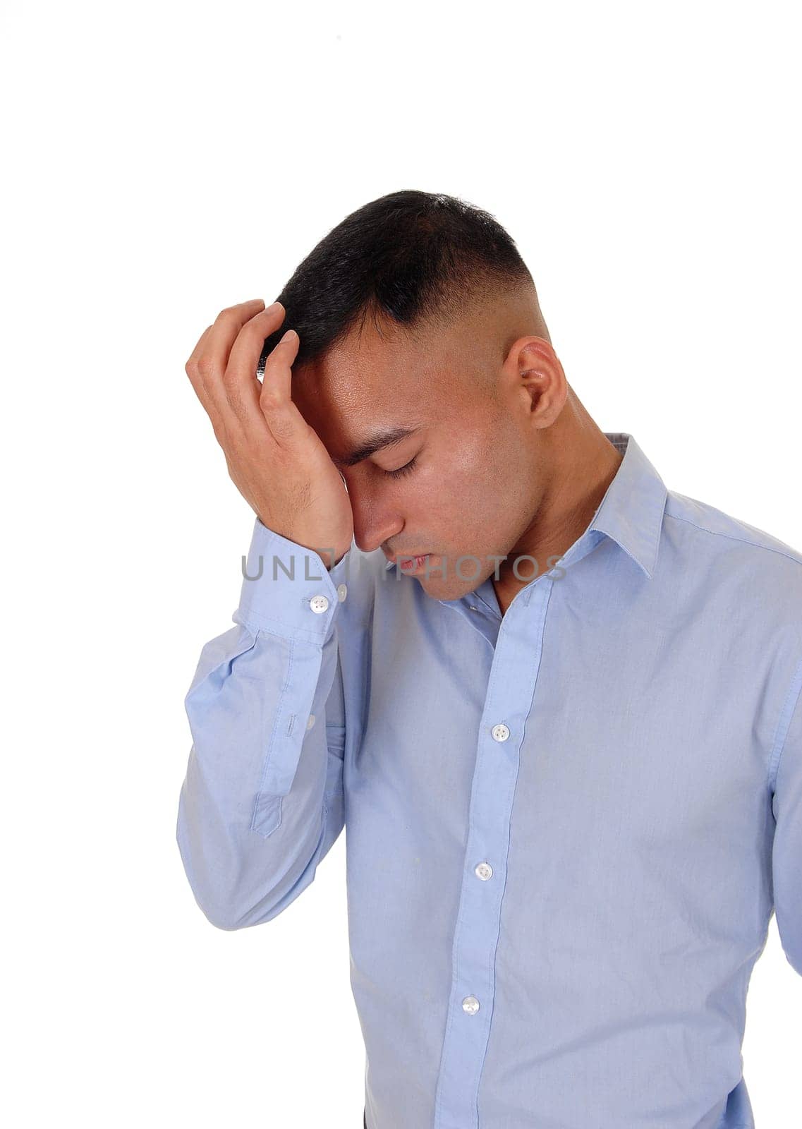A handsome east Indian business man standing in the studio isolated.over white background, in a blue shirt with one hand on his forehead.thinking hard.