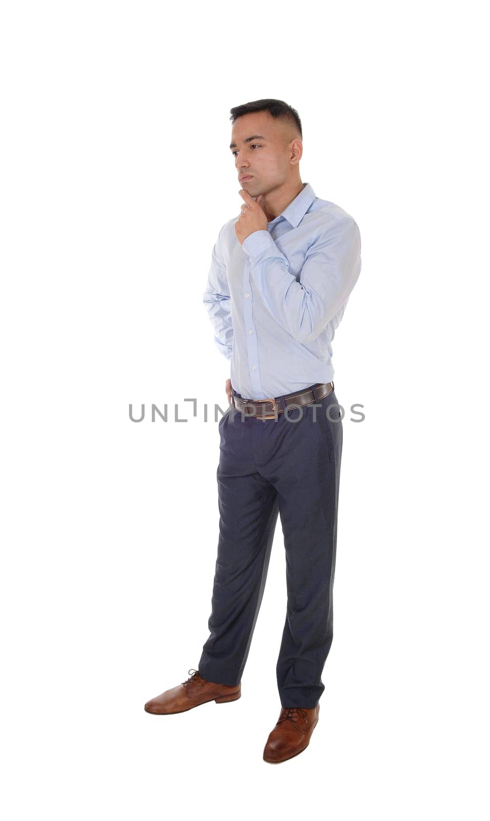 A handsome young east Indian man standing in a blue shirt with his.one hand under his chin, thinking, isolated for white background.