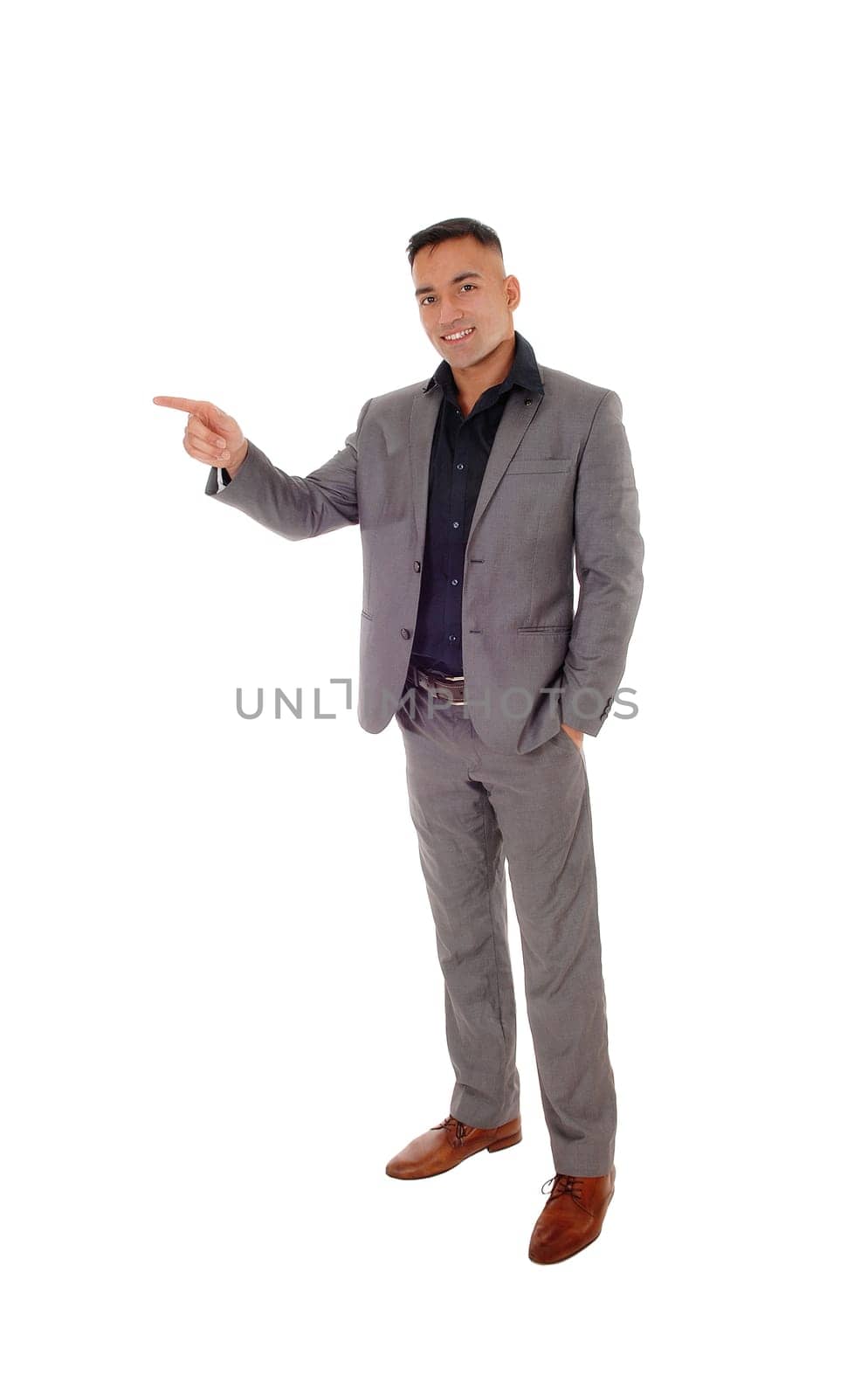 A handsome young man standing with his hands in his pocket in a gray.suit, pointing with one hand, isolated for white background.