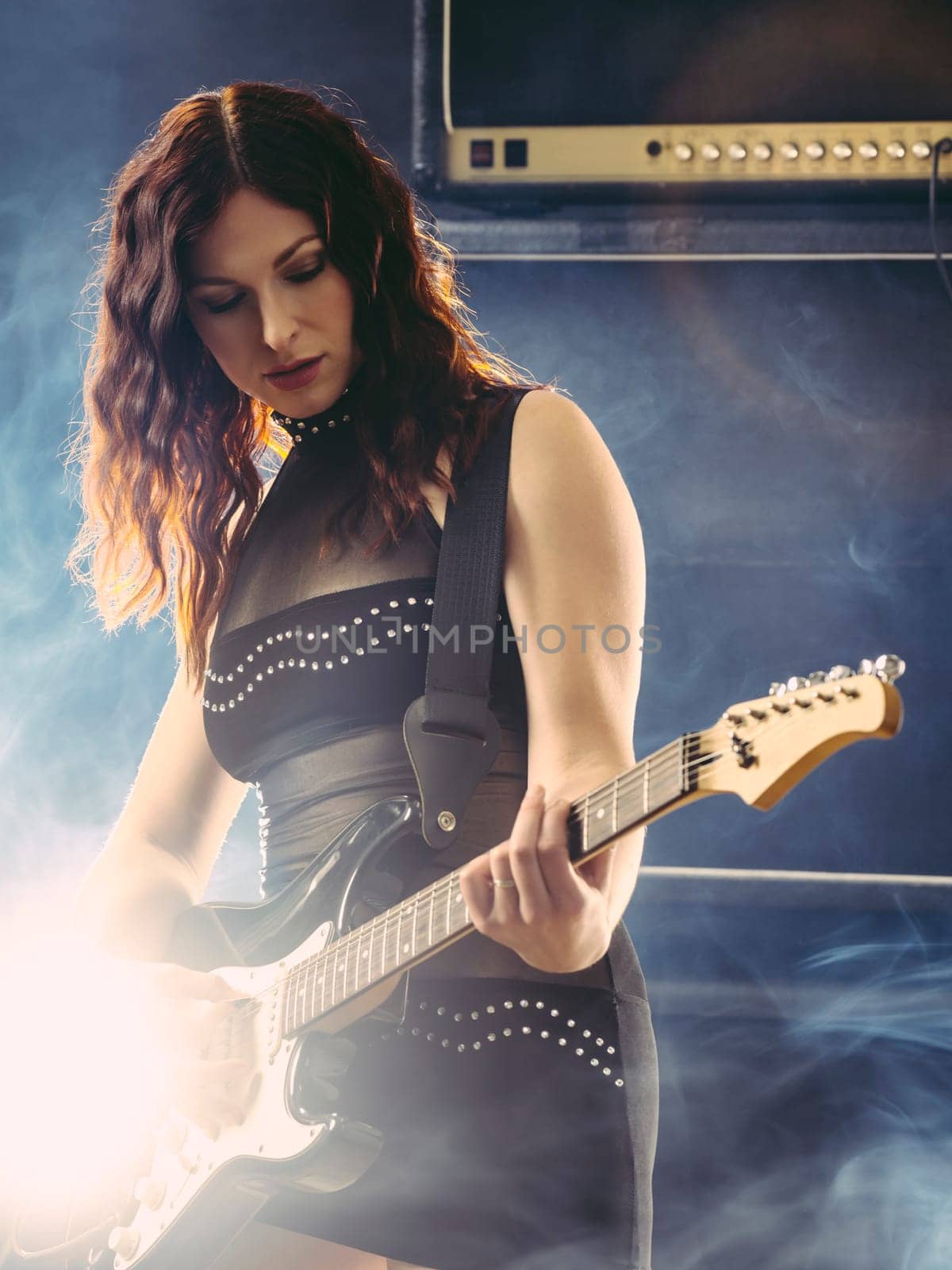 Young beautiful redhead woman playing an electric guitar in front of large amplifier.