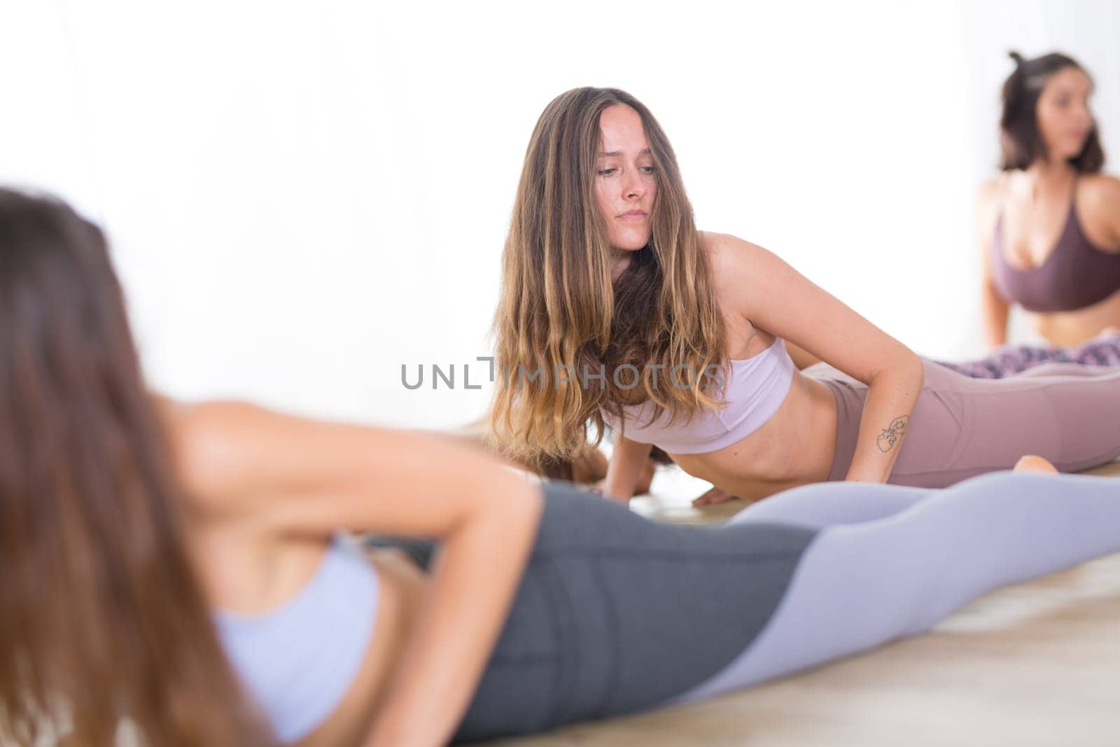 Group of young sporty attractive women in yoga studio, practicing yoga lesson with instructor, stretching and relaxing after workout . Healthy active lifestyle, working out indoors in gym.