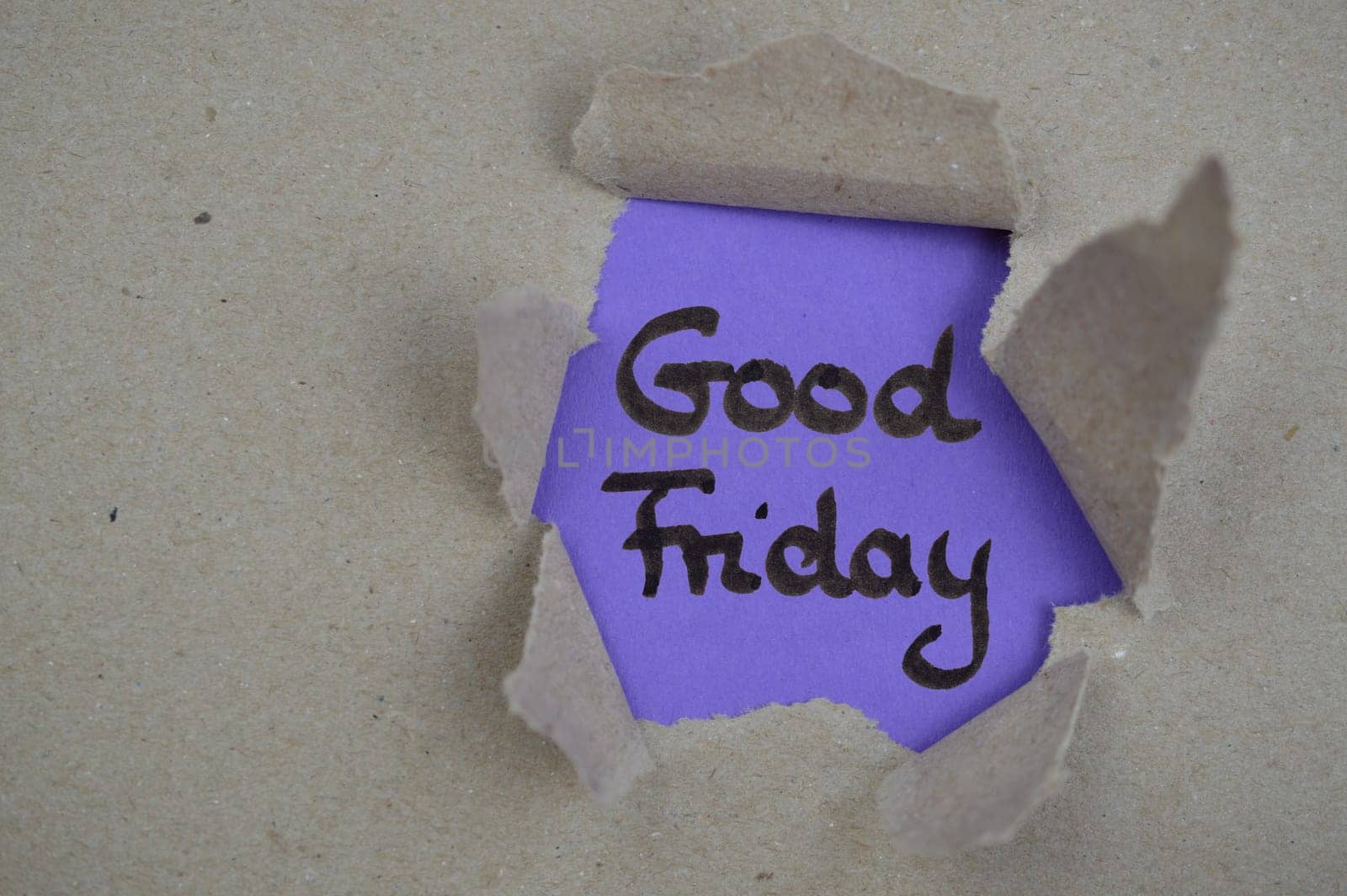 The words Good Friday on purple paper beneath ripped open gray packing paper visible through a hole