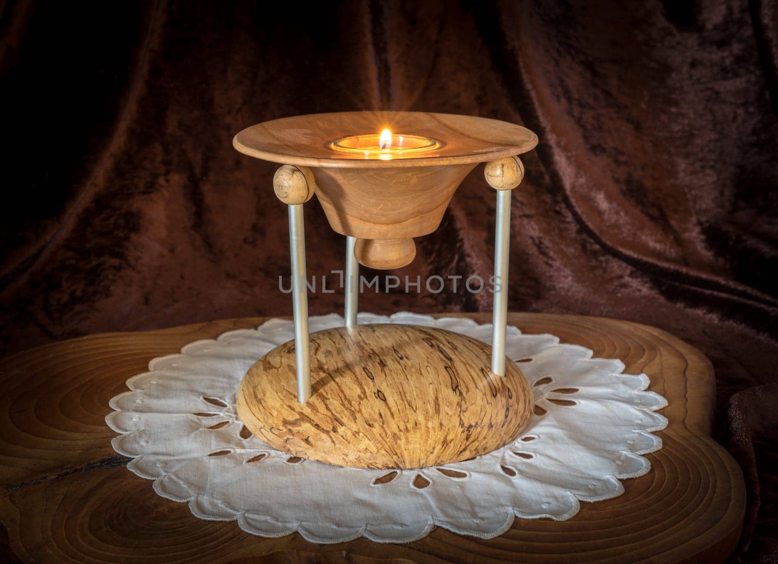 Multi-part wooden candlestick with burning candle stands on a dark wooden board against brown background
