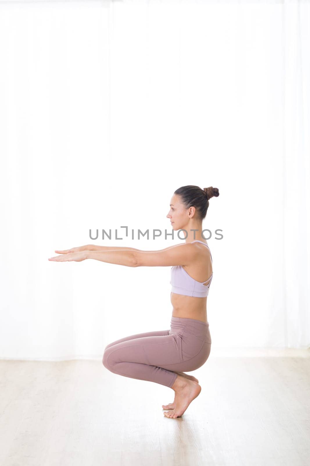 Portrait of gorgeous active sporty young woman practicing yoga in studio. Beautiful girl practice Utkatasana, awkward yoga pose. Healthy active lifestyle, working out in gym.