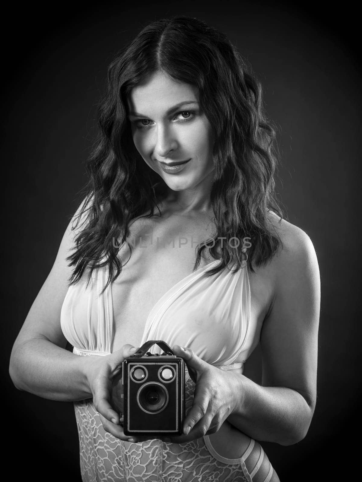 Beautiful happy woman wearing lingerie holding retro camera.