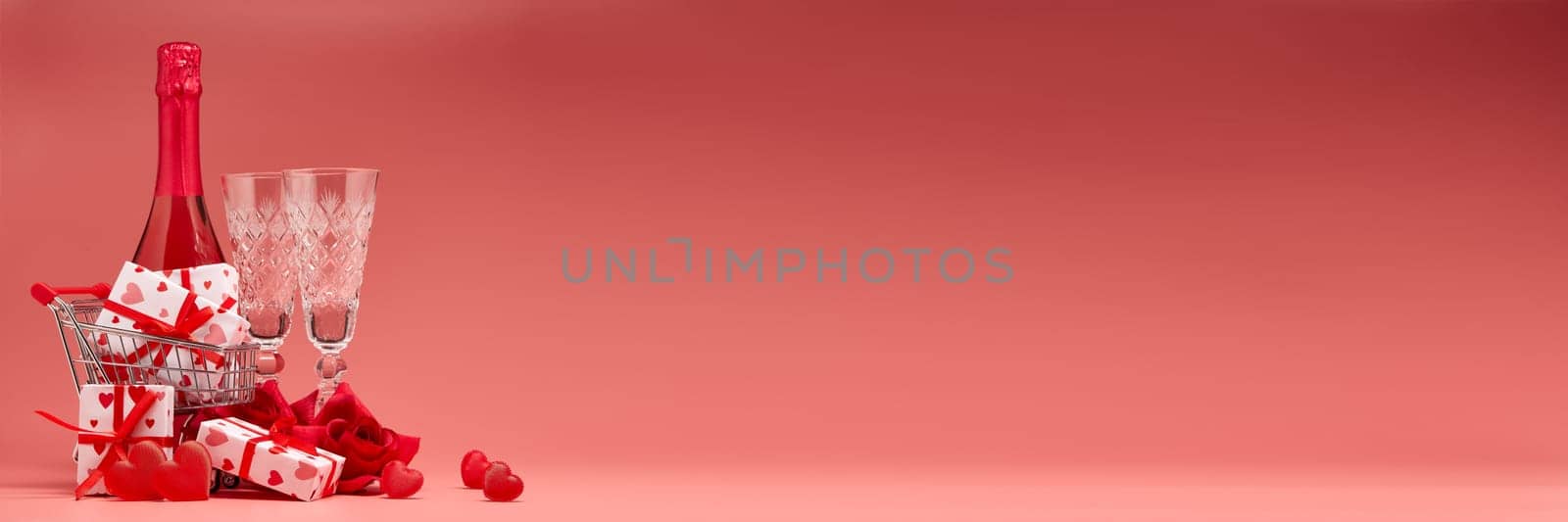 Shopping trolley, gift boxes, red roses and hearts, champagne and flutes on pink background with copy space. Valentine's Day. Festive background with decorative hearts.Valentine's Day. Wedding day.