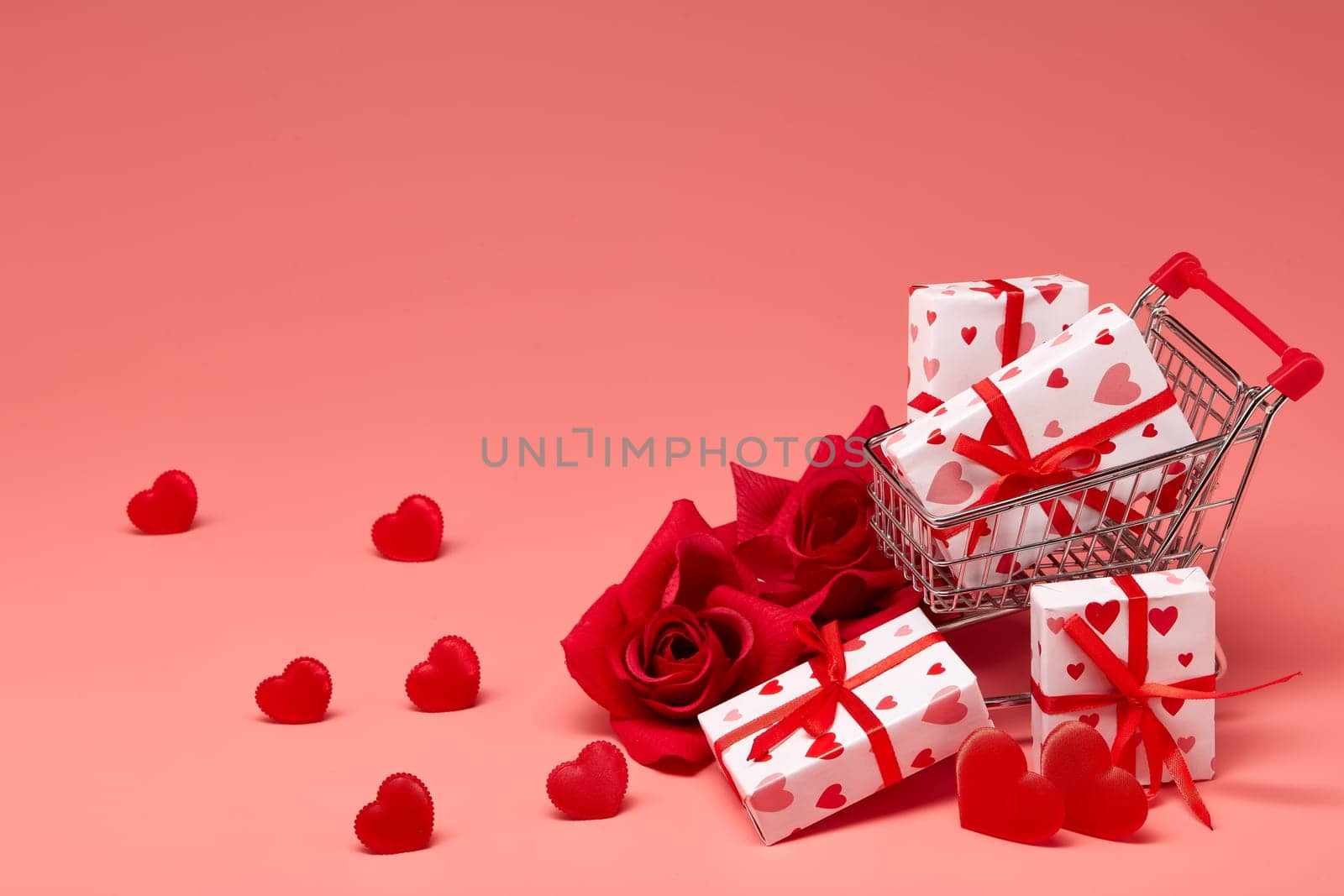 Shopping trolley with gift boxes, red roses and hearts on pink background with copy space. Festive background with decorative hearts.Valentine's Day. Wedding day.