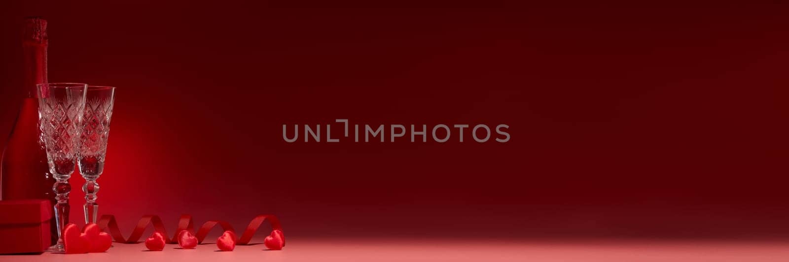 Red hearts, gift box, champagne bottle and flutes on red background. Copy space. Valentine's Day. Wedding Day. For romantic greeting card, invitation. Extra wide panorama banner background