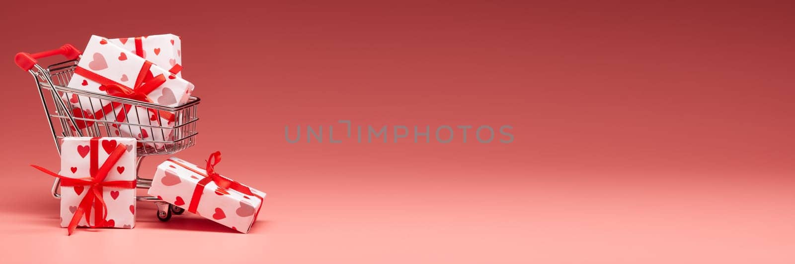 Shopping trolley with gift boxes on pink background with copy space. Valentine's Day. Mother's day, wedding, women's day. Extra wide panorama banner background