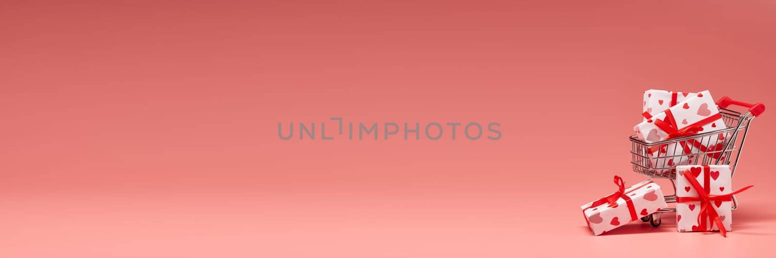 Shopping trolley with gift boxes on pink background with copy space. Valentine's Day. Mother's day, wedding, women's day. Extra wide panorama banner background